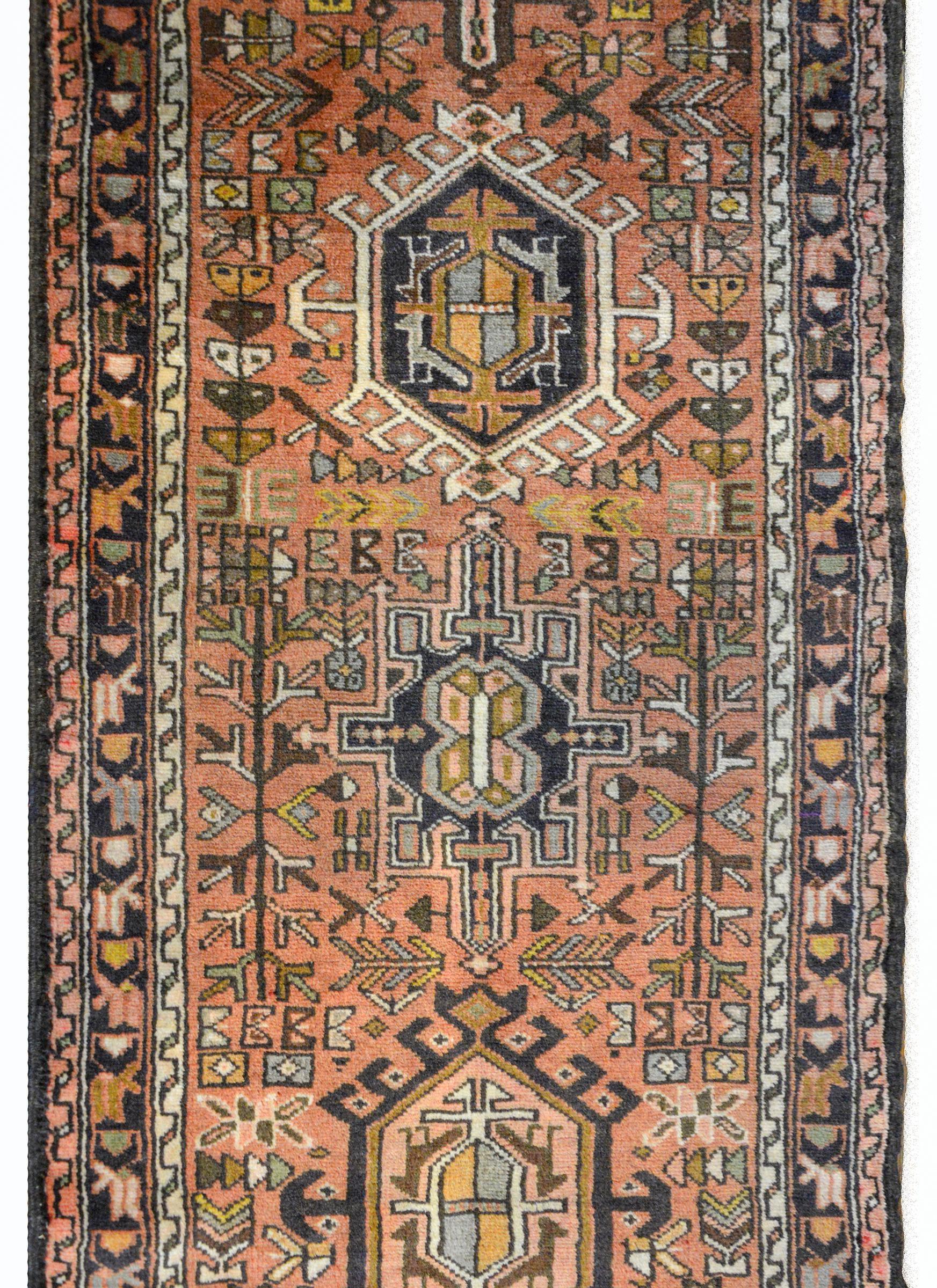 A wonderful mid-20th century Persian Karadja runner with several stylized floral medallions woven in myriad colors including brown, coral, pink, white, gold, and black, amidst a field of more stylized flowers against a coral background. The border