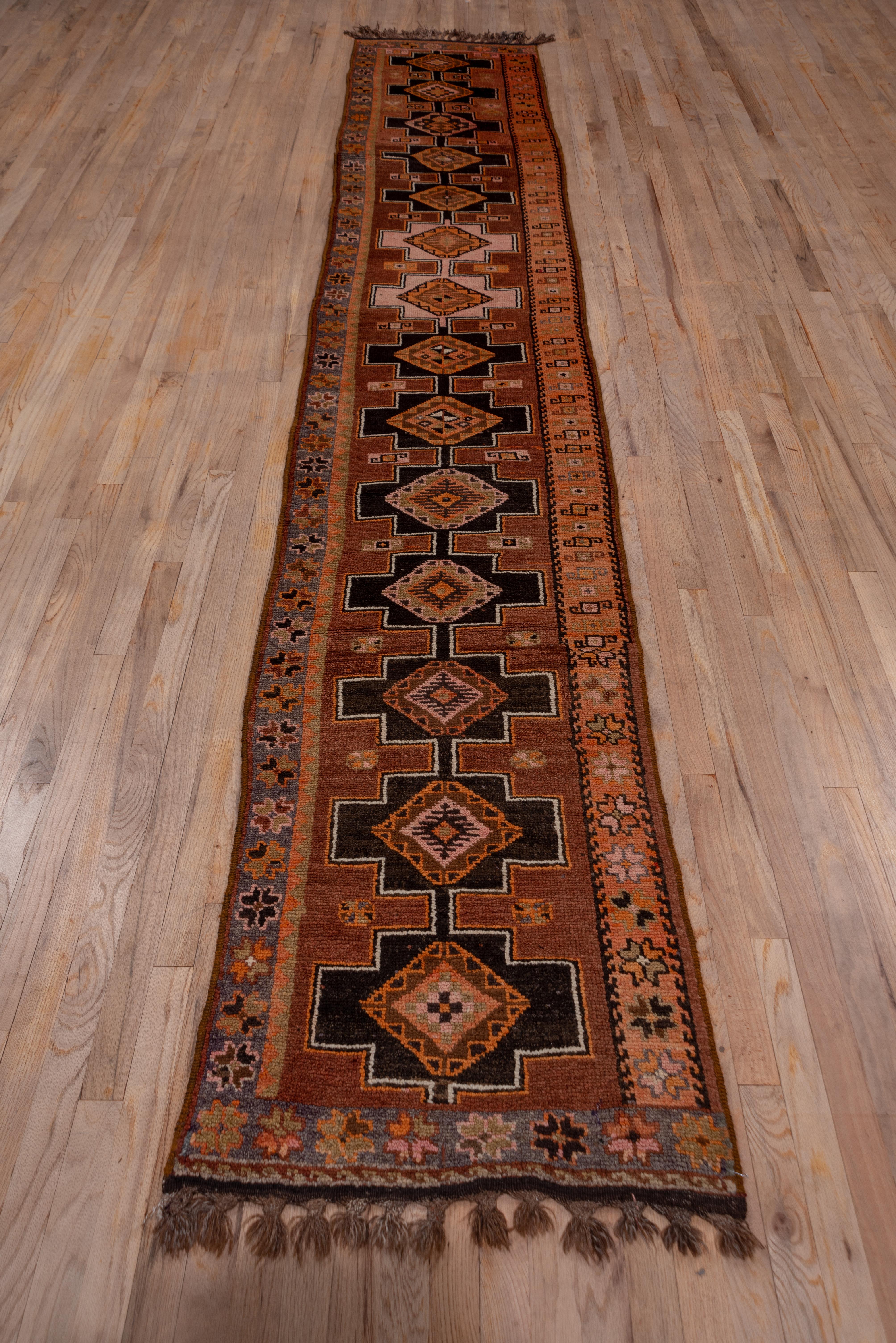 This narrow northeastern Turkish kenare features a soft coral field with a pole medallion of conjoint dark brown or ivory stepped rectangles, each enclosing a stepped lozenge in red, soft rust, pale green and dark brown. The end abrashed yellow