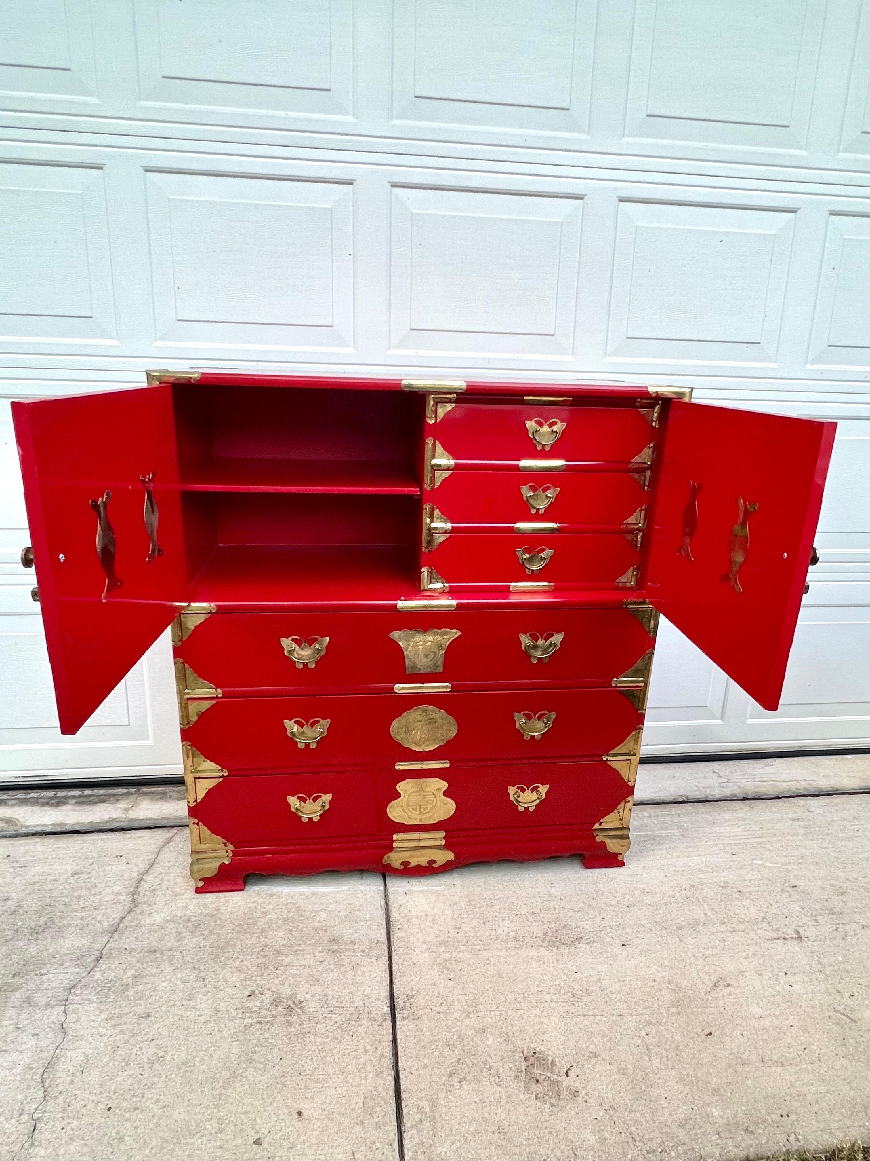 Mid-20th century brass mounted red lacquered sideboard / tansu campaign chest with profuse engraved brass butterfly and medallion mounts, two blind doors revealing 3 fitted interior upper drawers, and three lower long drawers. Does not have