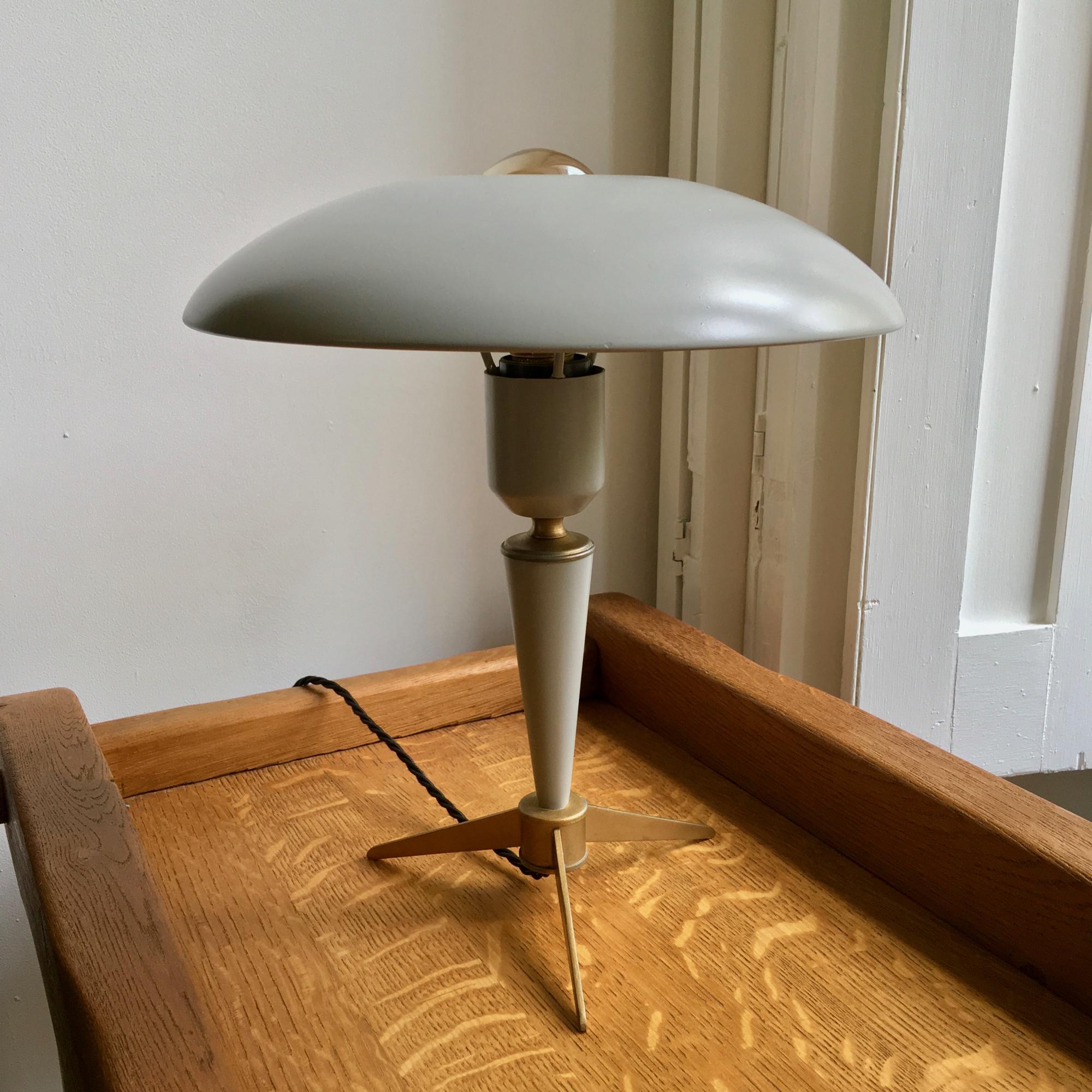 Small midcentury table lamp with tripod base by Louis Kalff for the Dutch manufacturer Philips.

A very nice design which channels light above and below the shade, often shown with a chrome or gold crown bulb to shield the light from above the