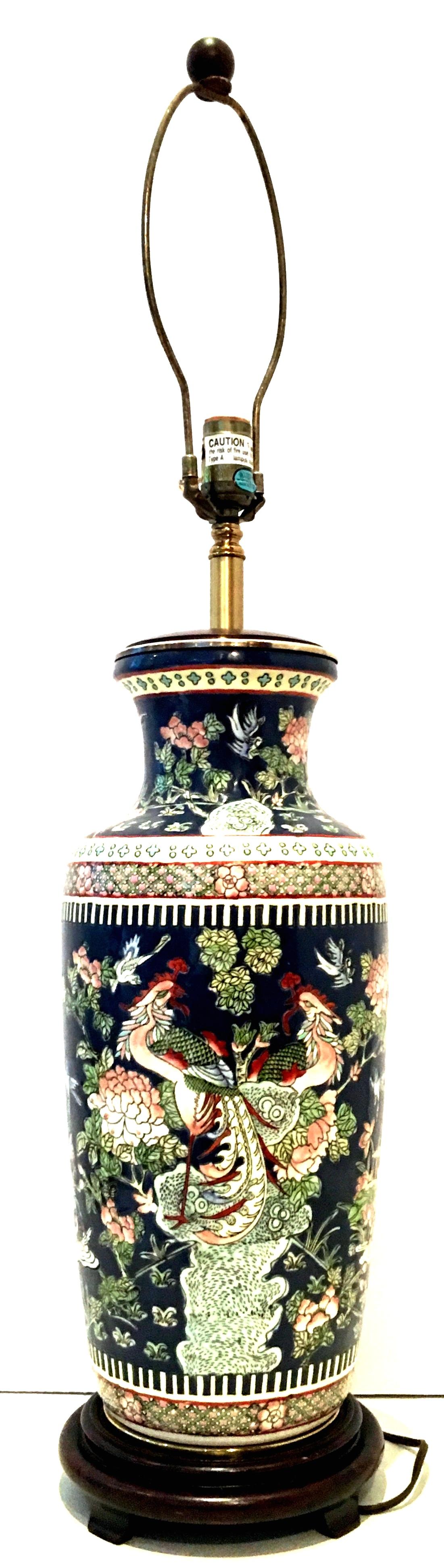 Mid-20th Century large Famille hand painted porcelain and brass wood mounted lamp. This finely crafted hand painted lamp features a navy blue ground with green, pink, robins egg blue, red and yellow peacock, flora, birds, eggs and ducks motif.