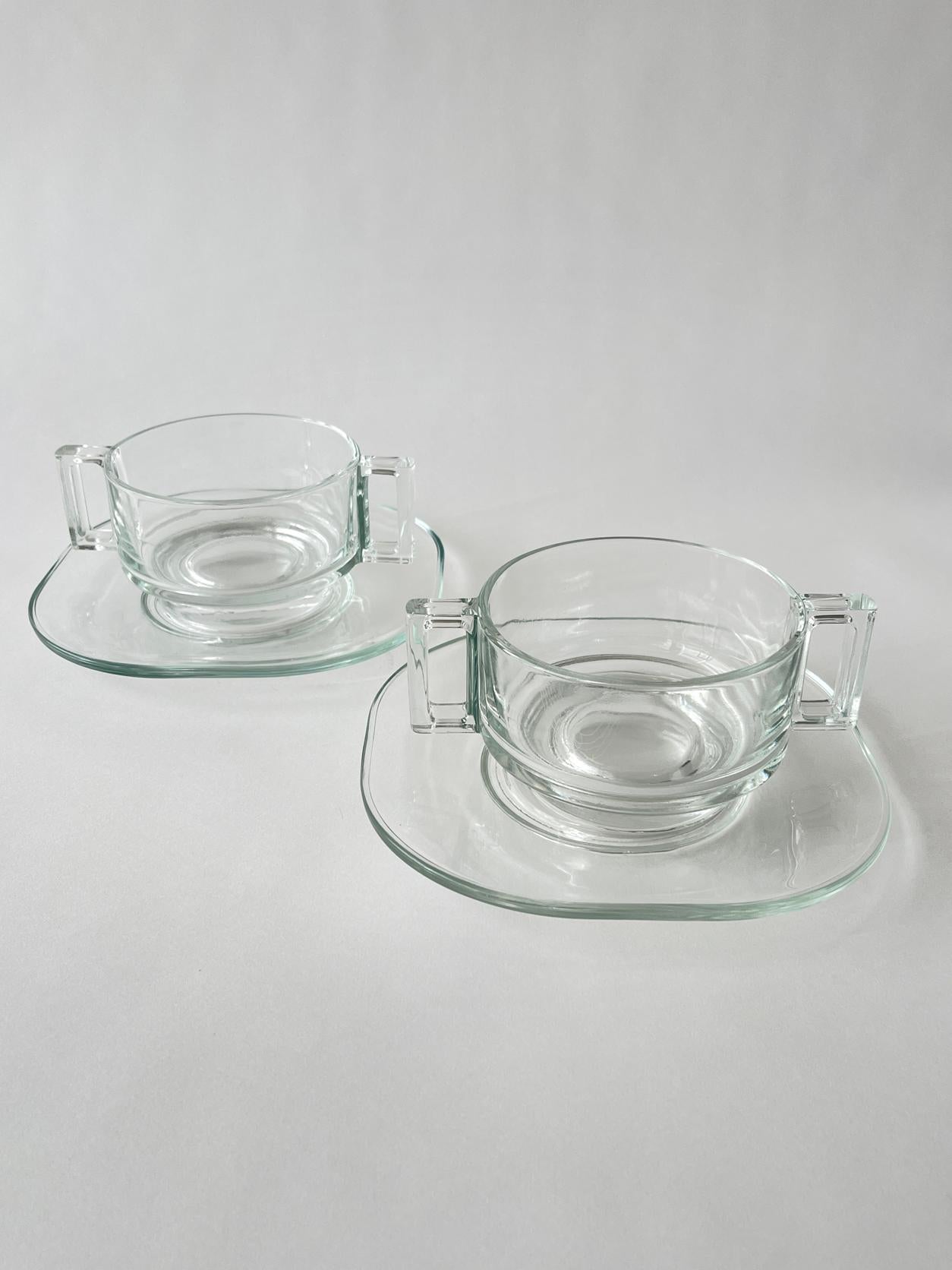 20th century Joe Colombo double handled cup and saucer set with an iconic design including a cylinder tiered body and rectangular handles. Clean and sophisticated. Sold as two sets(2 mugs and 2 saucers).

Measures: 7.25