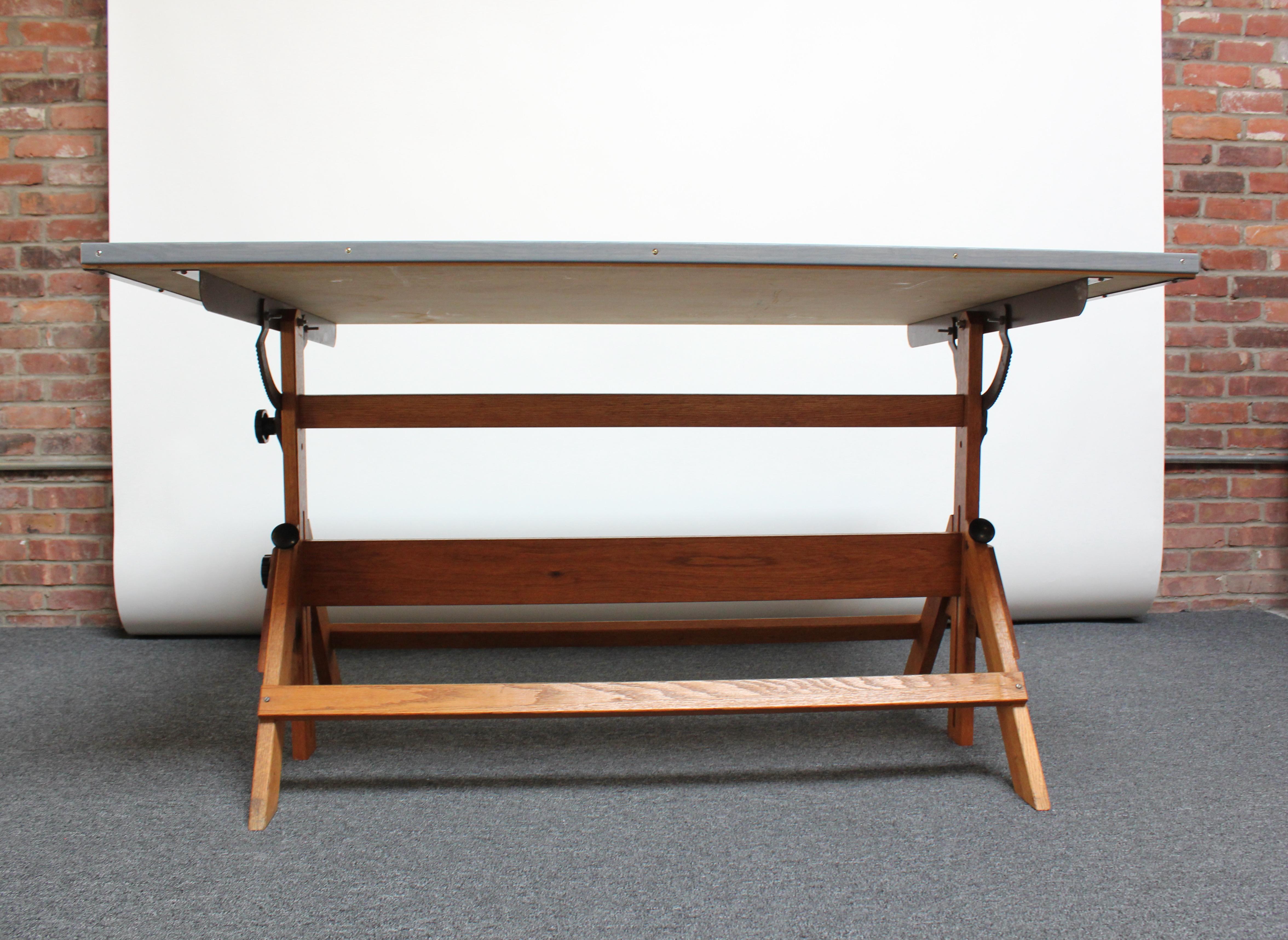 Large drafting table (ca. 1950s, USA) composed of a maple surface with gray and brown painted trim supported by an oak base. 
Surface has been refinished; light wear remains as shown to the surface and border (few scuffs). There are also a few