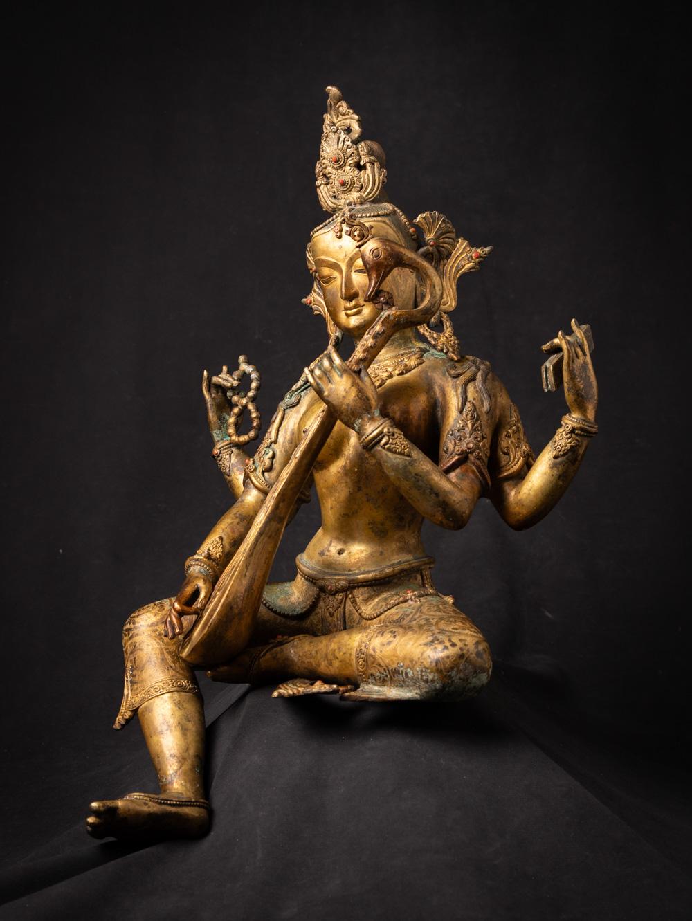 The large old bronze Nepali Saraswati statue is a truly magnificent and spiritually significant artifact originating from Nepal. Crafted from bronze and fire gilded with 24-karat gold, this statue stands tall at 54 cm in height and measures 35.5 cm