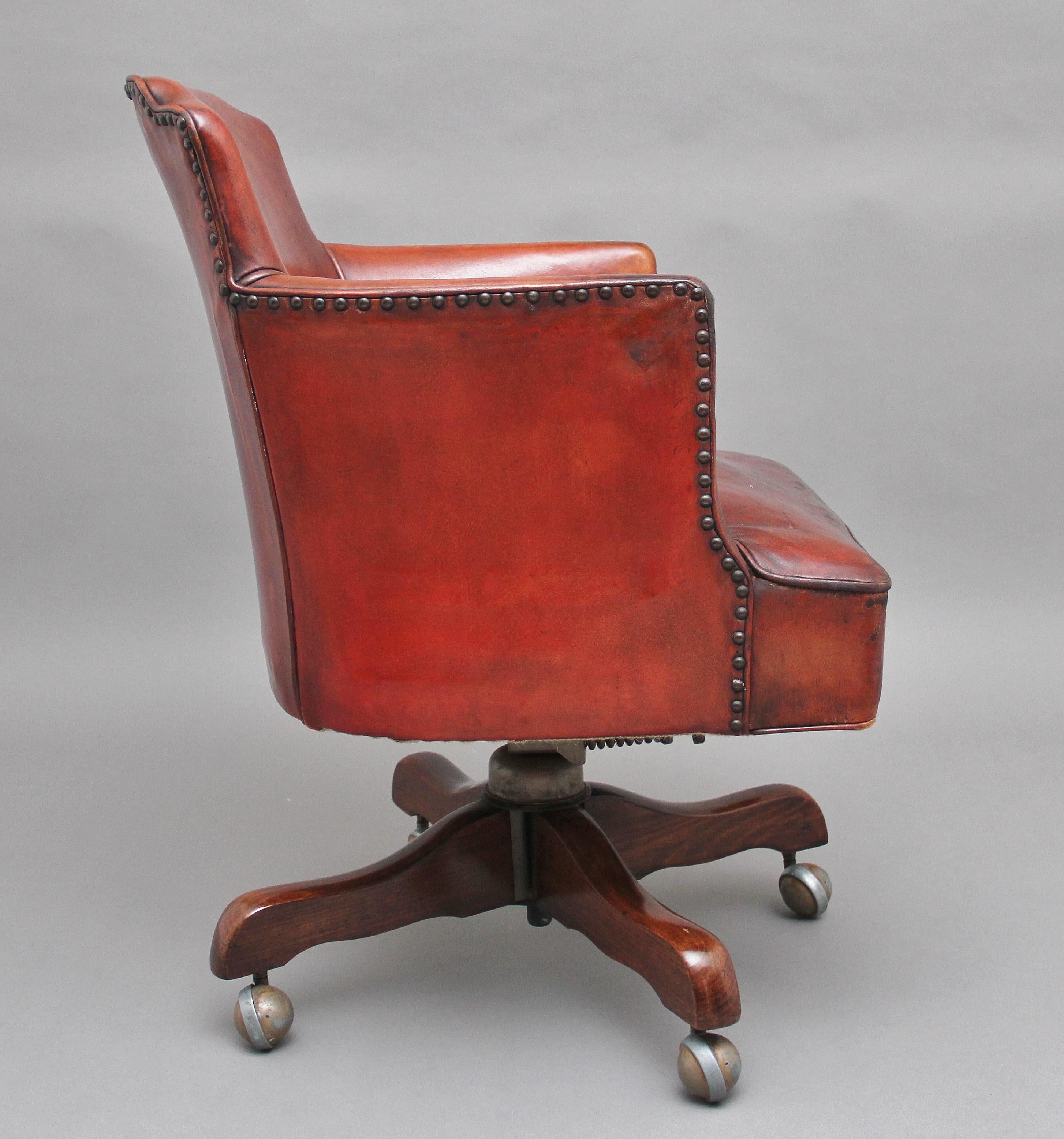Mid-20th century leather swivel desk chair in a nice deep red color, having a shaped back, cushioned seat and having brass stud decoration, supported on a beech base, circa 1950.
   