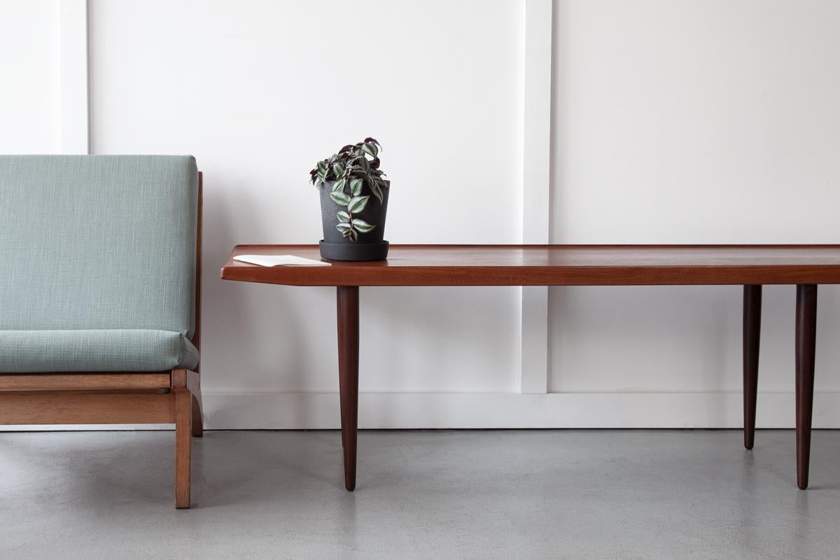 An elegant Danish coffee table in teak, with a classically minimalist style, standing on tapering legs with lipped edges and richly grained surface. 