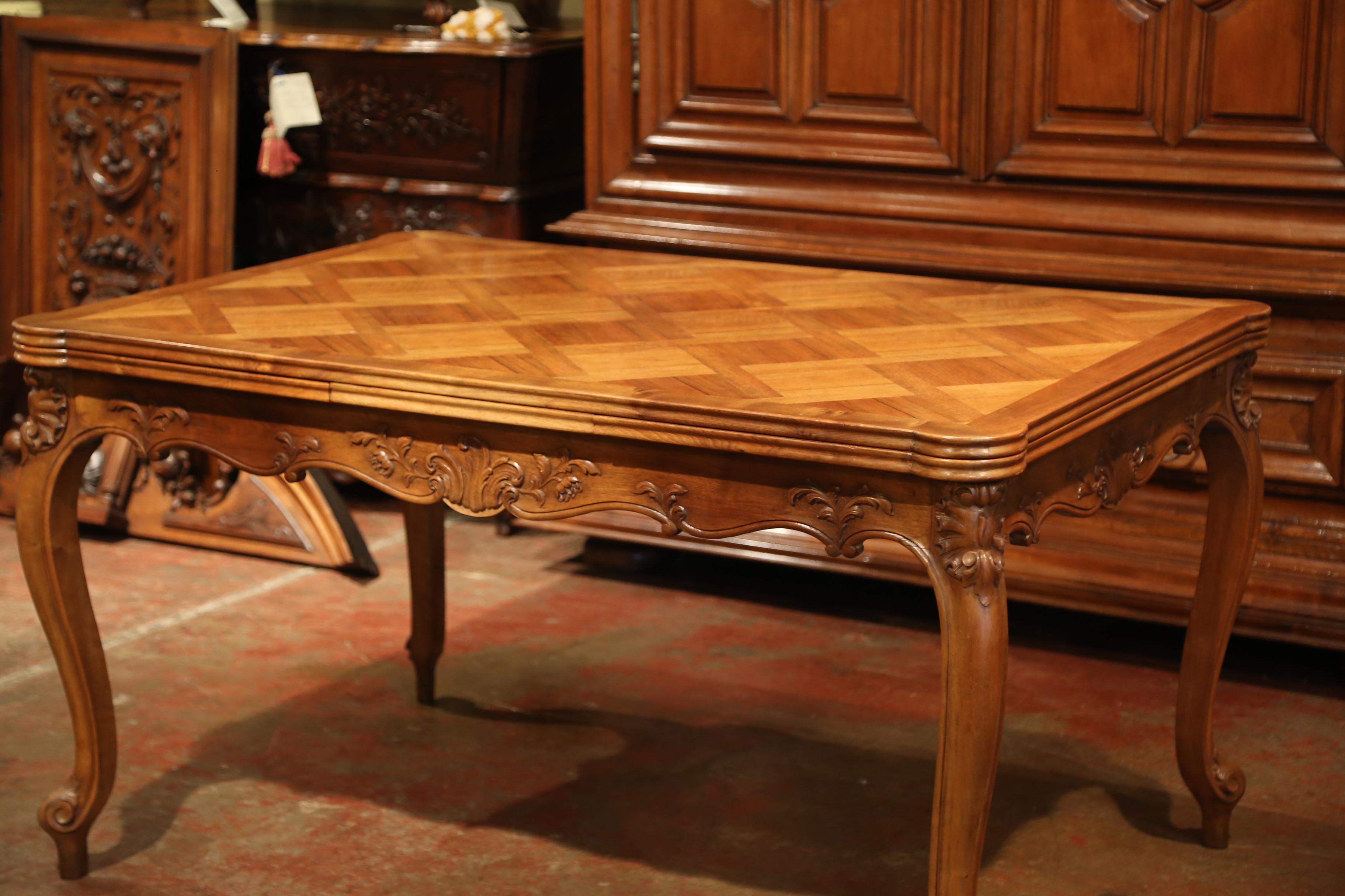 This elegant, antique dining table is a true eyecatcher! Crafted in Provence circa 1950, this fruitwood refectory table has four cabriole legs, a shaped apron with foliage motifs, and a parquetry top with beautiful, geometric details. Under the top