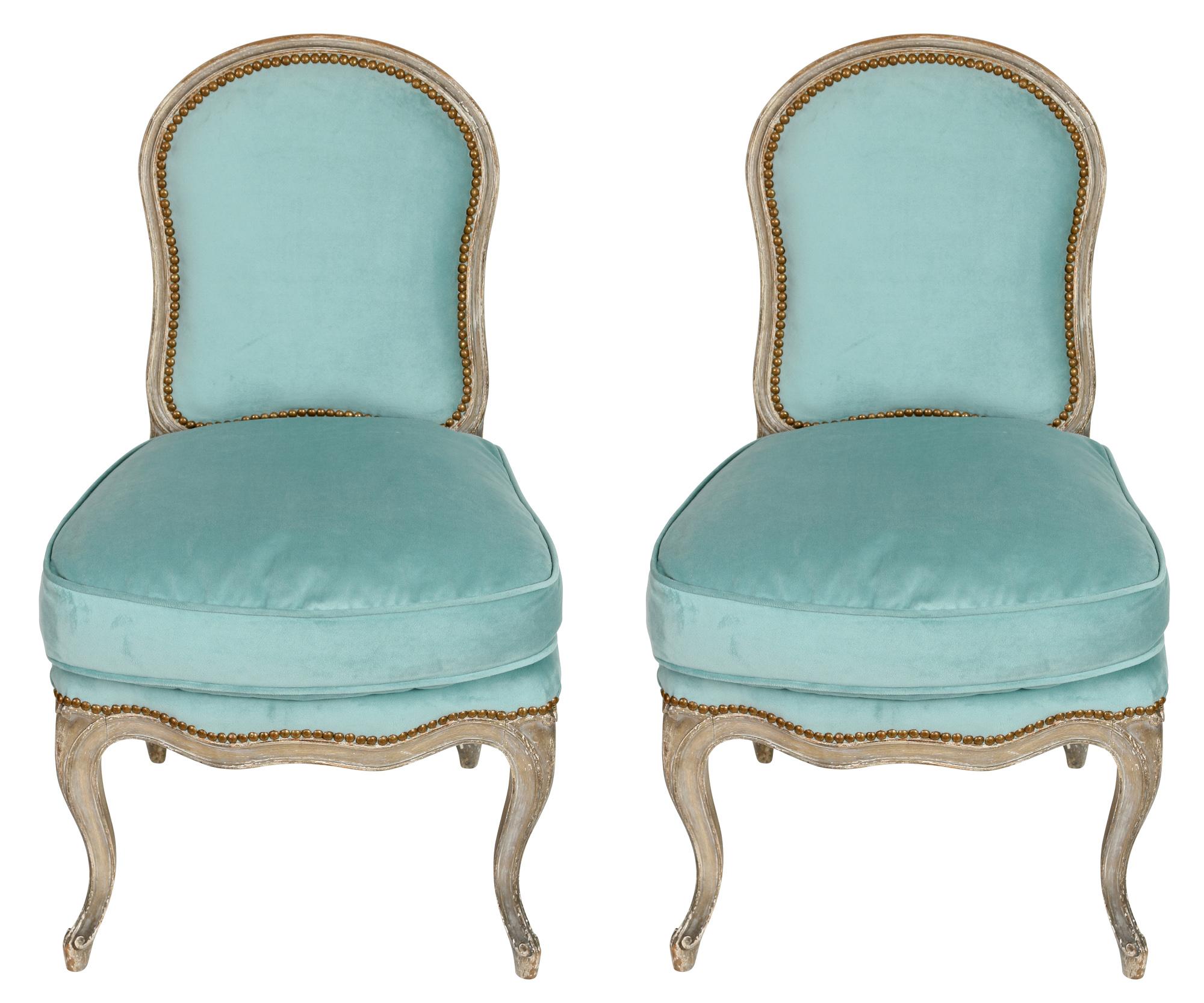 A charming pair of Louis XV style slipper chairs with a painted finish, a tight back and loose seat cushion, trimmed in nail heads. Upholstered in a lovely blue, this duo would be perfect as extra seating in living room or accent chairs in a bedroom