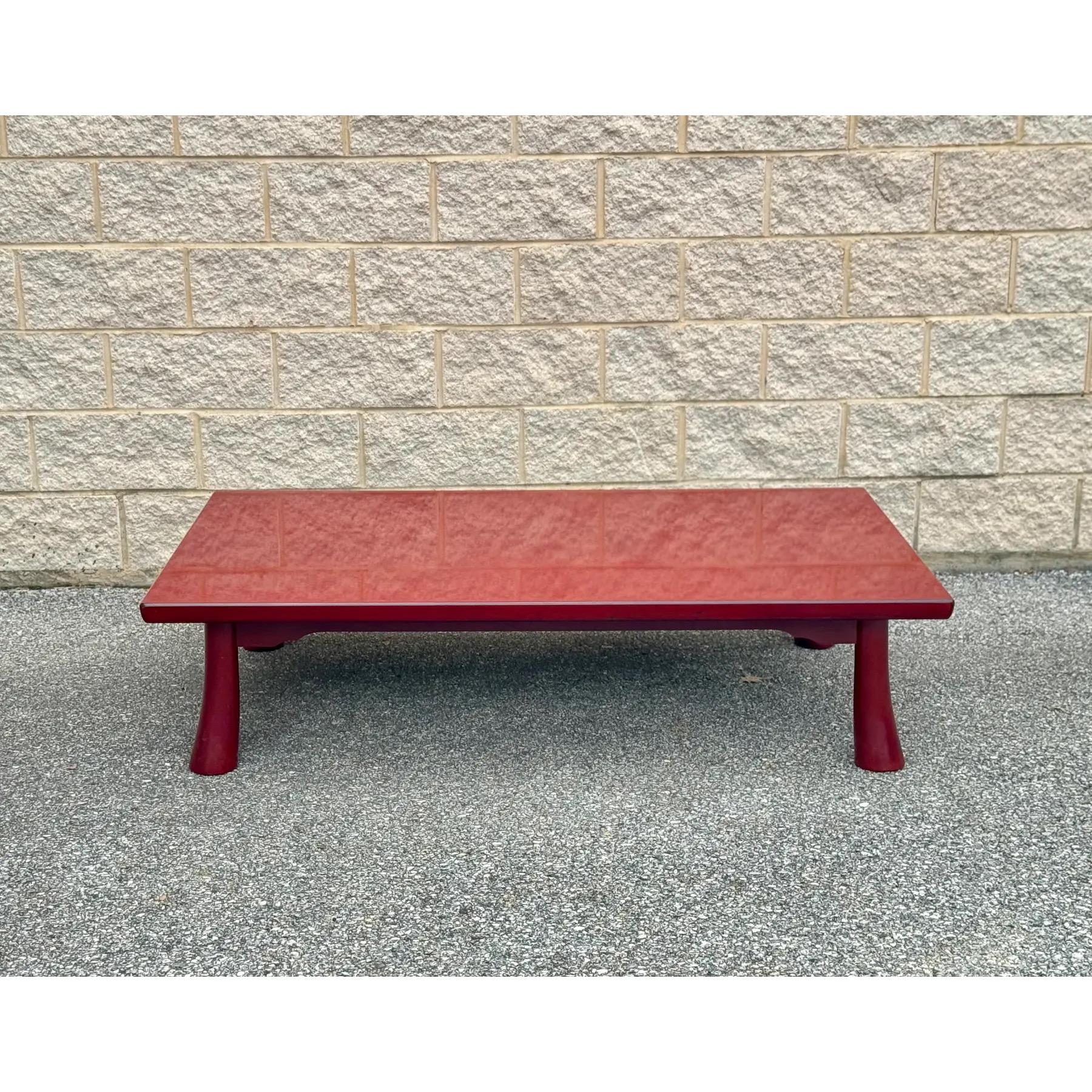 Table basse en laque rouge avec un motif répétitif sous la surface. Le plateau laqué lisse présente un design complexe et tourbillonnant qui recouvre l'ensemble de la table, caractéristique de l'artisanat asiatique traditionnel. 

