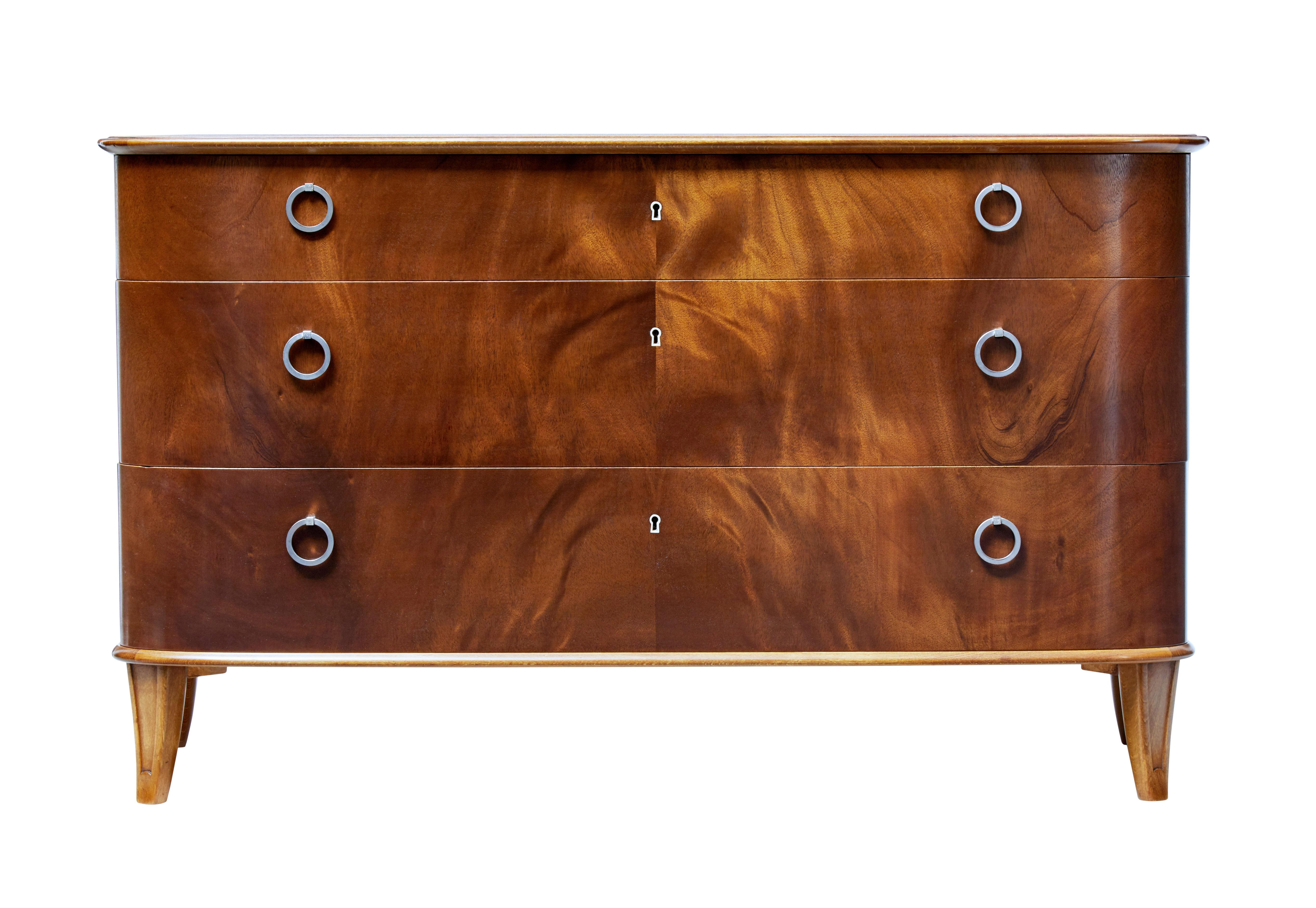Fine quality shaped chest of drawers by Swedish retailers Svensk Mobelindustri, circa 1950.

Presented in excellent condition. Three graduating drawers with flame mahogany fronts. Fitted with steel ring handles.

Good rich color, standing on
