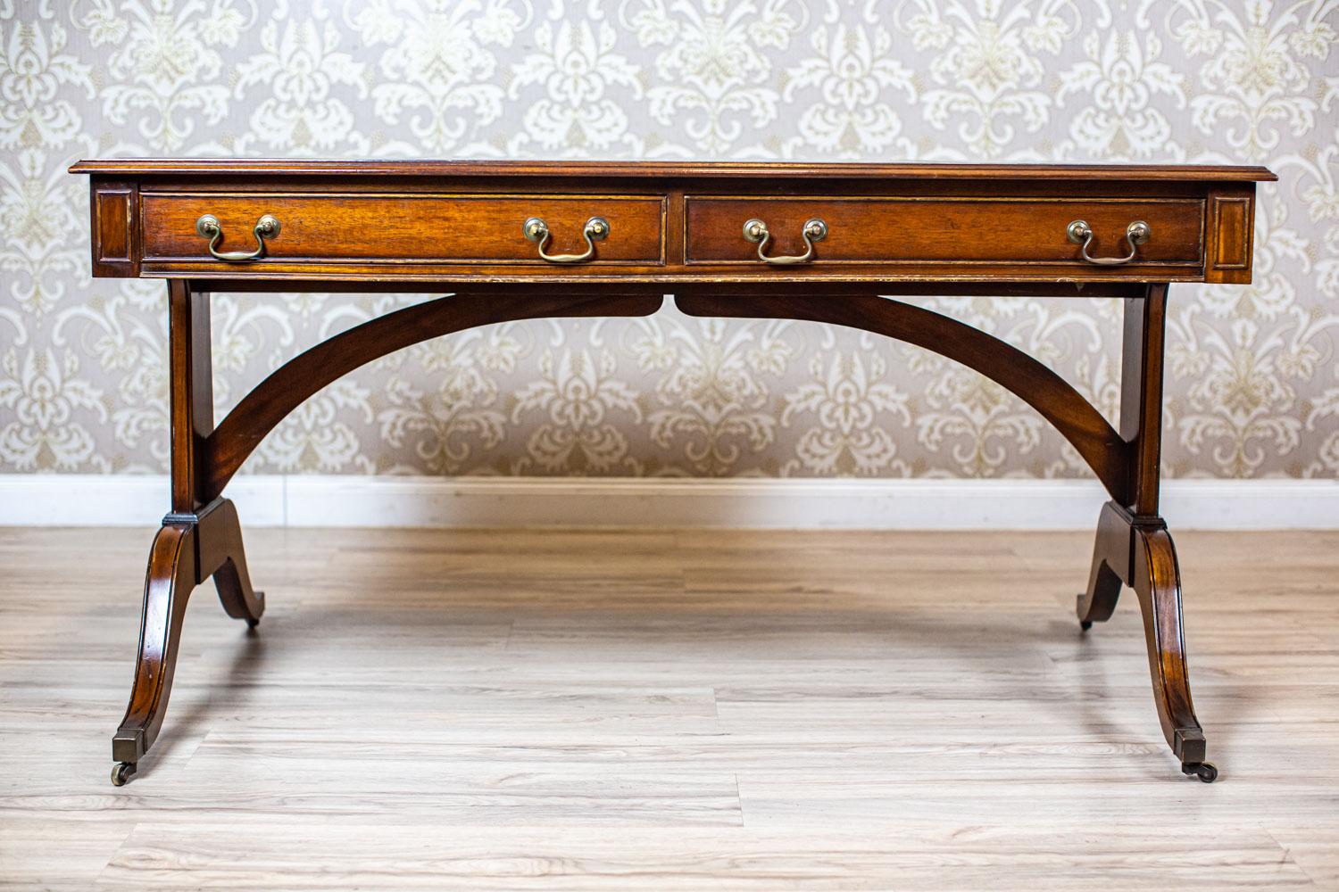 Mid-20th century mahogany desk in the English style

The desk top is wide, comfortable, and lined with leather. It hides two deep drawers, which help to optimize the work.
The desk legs are finished with metal rolls, so it is easier to move the