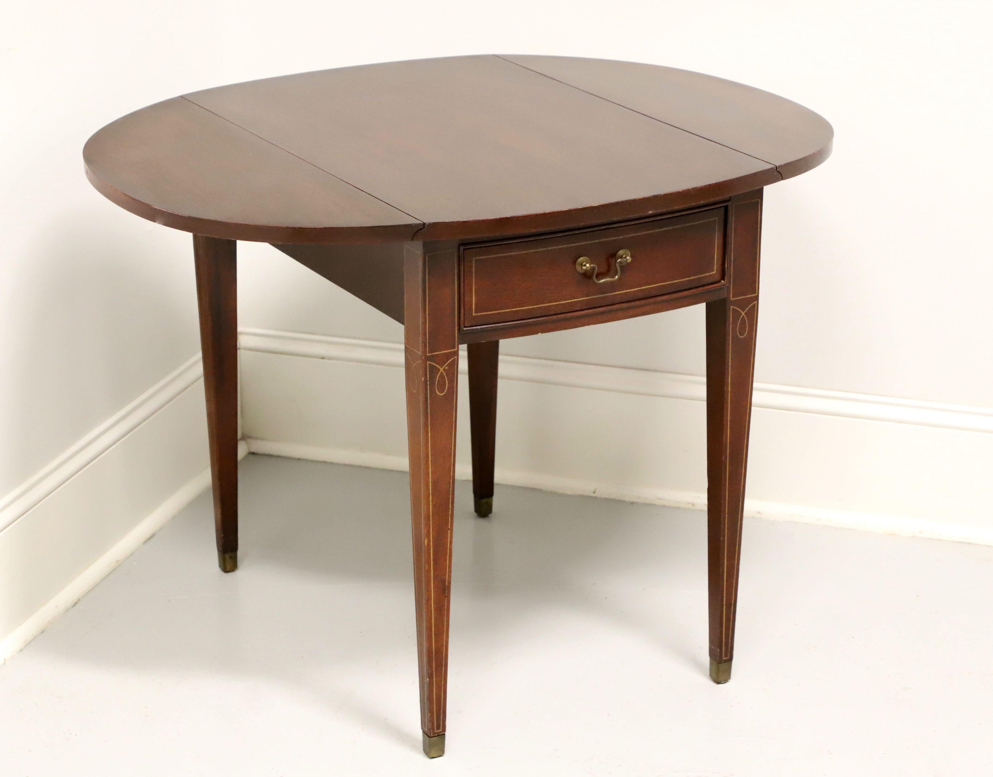 A Hepplewhite style Pembroke table, unbranded, similar in quality to Drexel and Hickory Chair. Mahogany with inlaid details, drop leaves, brass hardware, tapered straight legs and brass toe caps. Features one drawer of dovetail construction. Made in