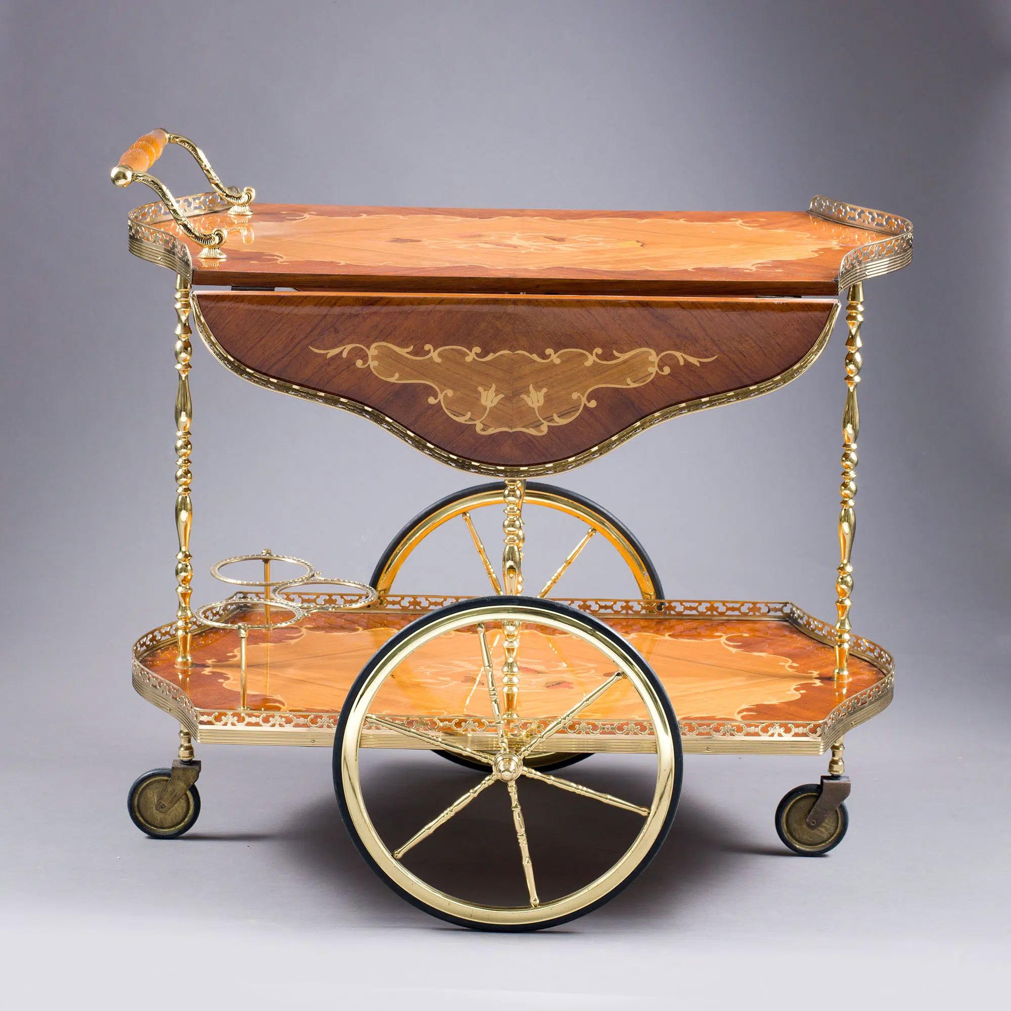 Mid-20th century marquetry and polished brass drinks trolley, the upper tray with inlaid marquetry drop-leaves and pierced brass gallery, supported on lathe-turned solid brass legs, the lower level with marquetry tray and brass gallery, large