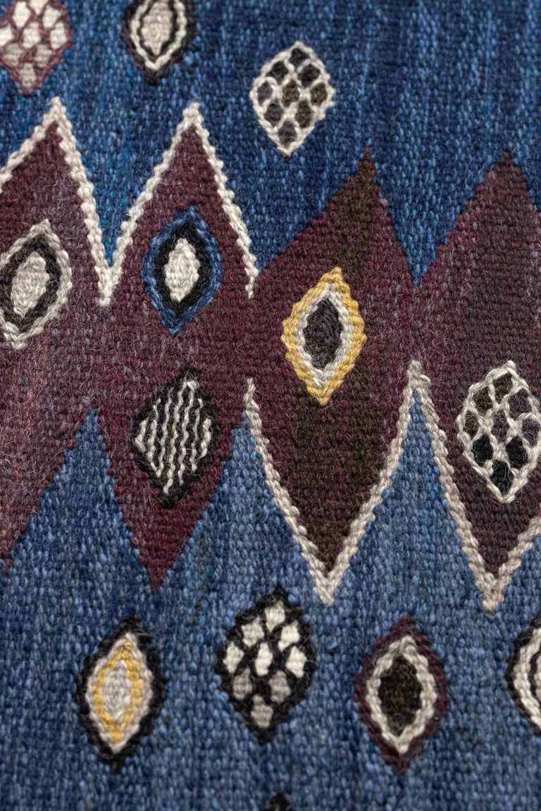 This vintage handwoven Swedish rug has a refined denim field with alternating shaded serrated columns overlaid with diagonal rows of scattered tribal motif, in a shaded denim border of similar motif. Signed by the original artist and