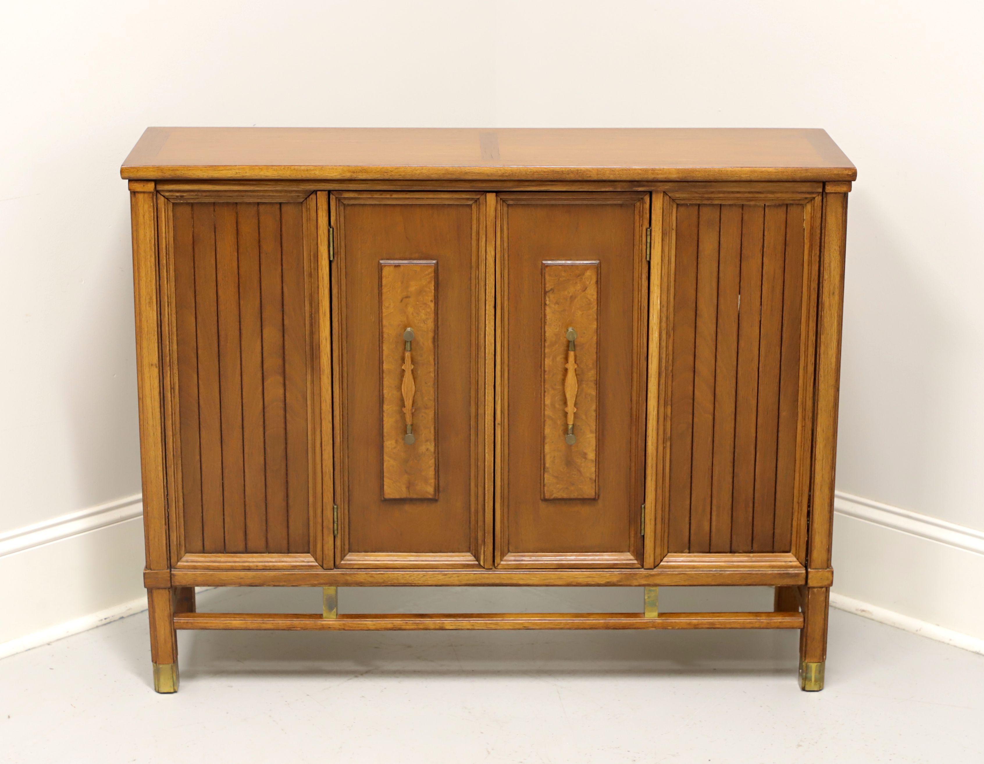 A mid 20th century modern narrow console cabinet, unbranded, similar quality to Century or Drexel. Walnut, burl to door fronts, with brass hardware and accents. Features a two door cabinet revealing a storage area with one fixed wood shelf. Made in