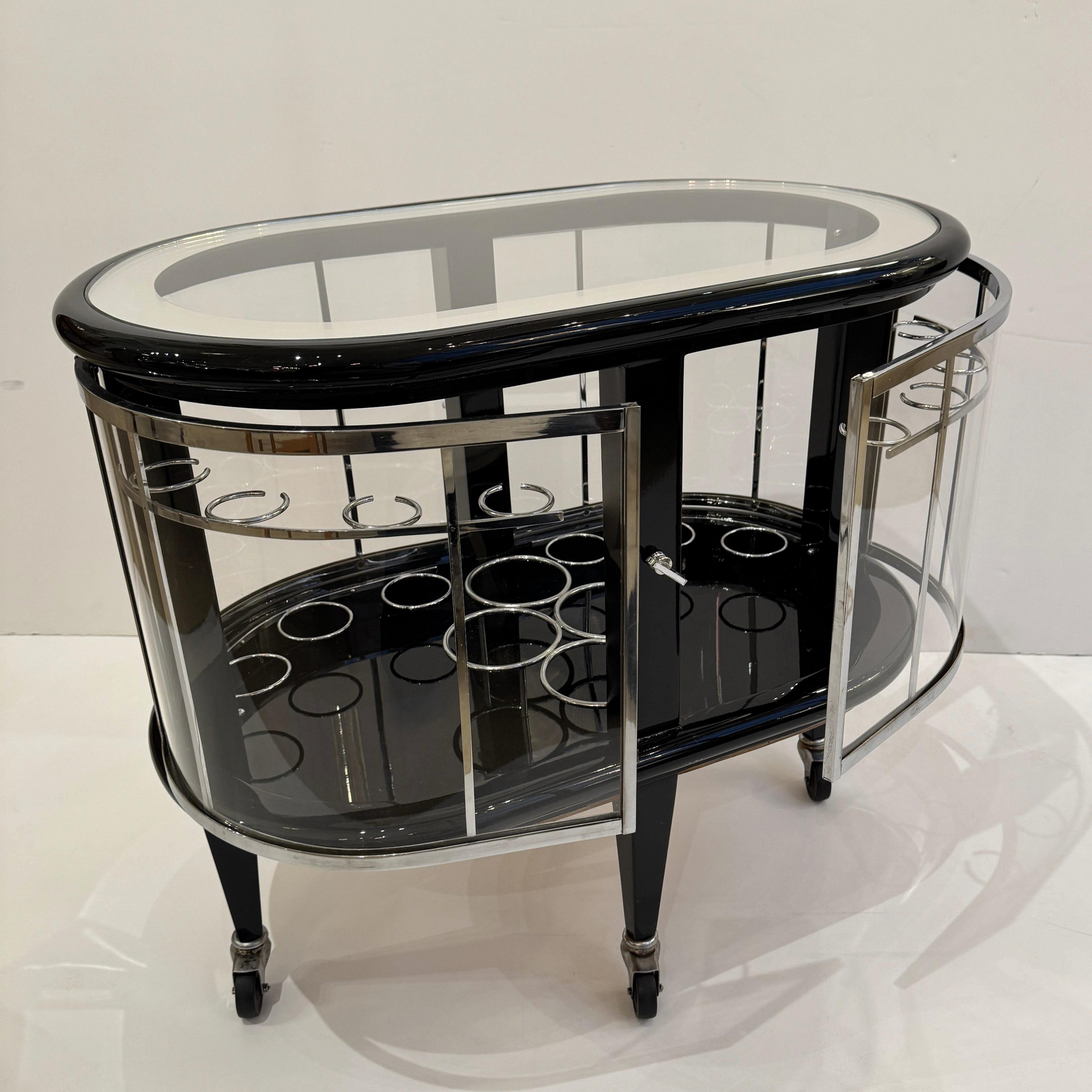 A Modernist ebonized bar cart. Black lacquer with polished nickel details, glass top with mirrored outer border and glass doors.