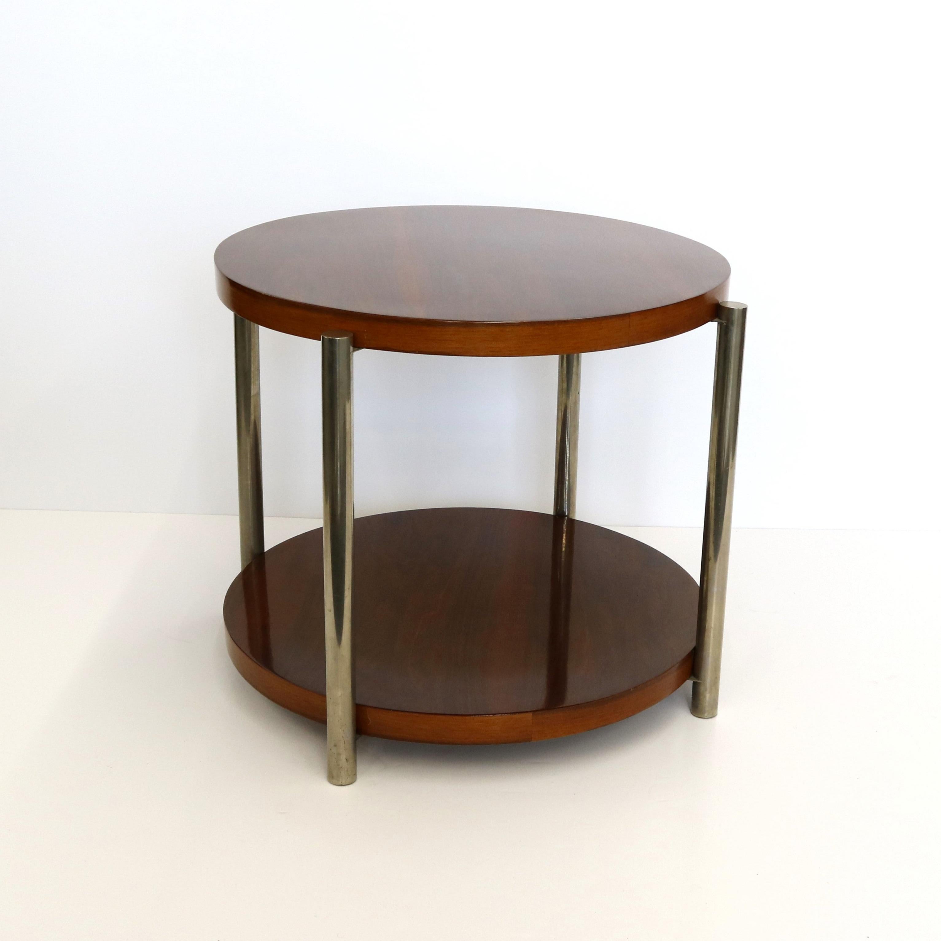 Table d'appoint moderniste, dotée d'un plateau circulaire emboîté dans des pieds tubulaires circulaires chromés.  Le plateau présente un riche motif de grain dans un magnifique placage de bois dur.  L'étagère inférieure reprend le design circulaire
