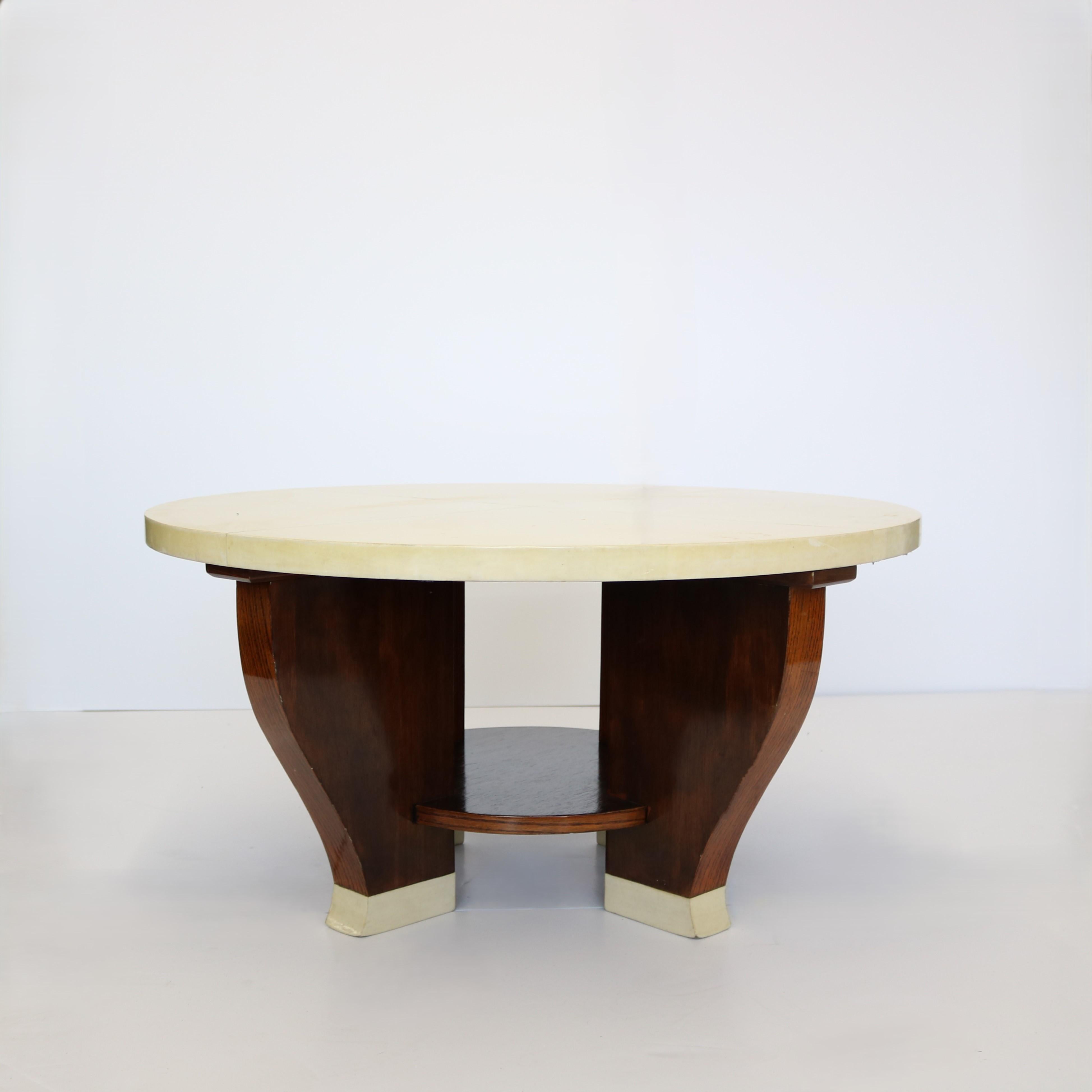 Bellissimo tavolo da cocktail circolare a due livelli in legno massiccio con piano rivestito in pergamena.  La base è composta da quattro gambe a forma di sciabola attenuata unite da una piattaforma centrale rotonda.  Anche i piedi di questo tavolo