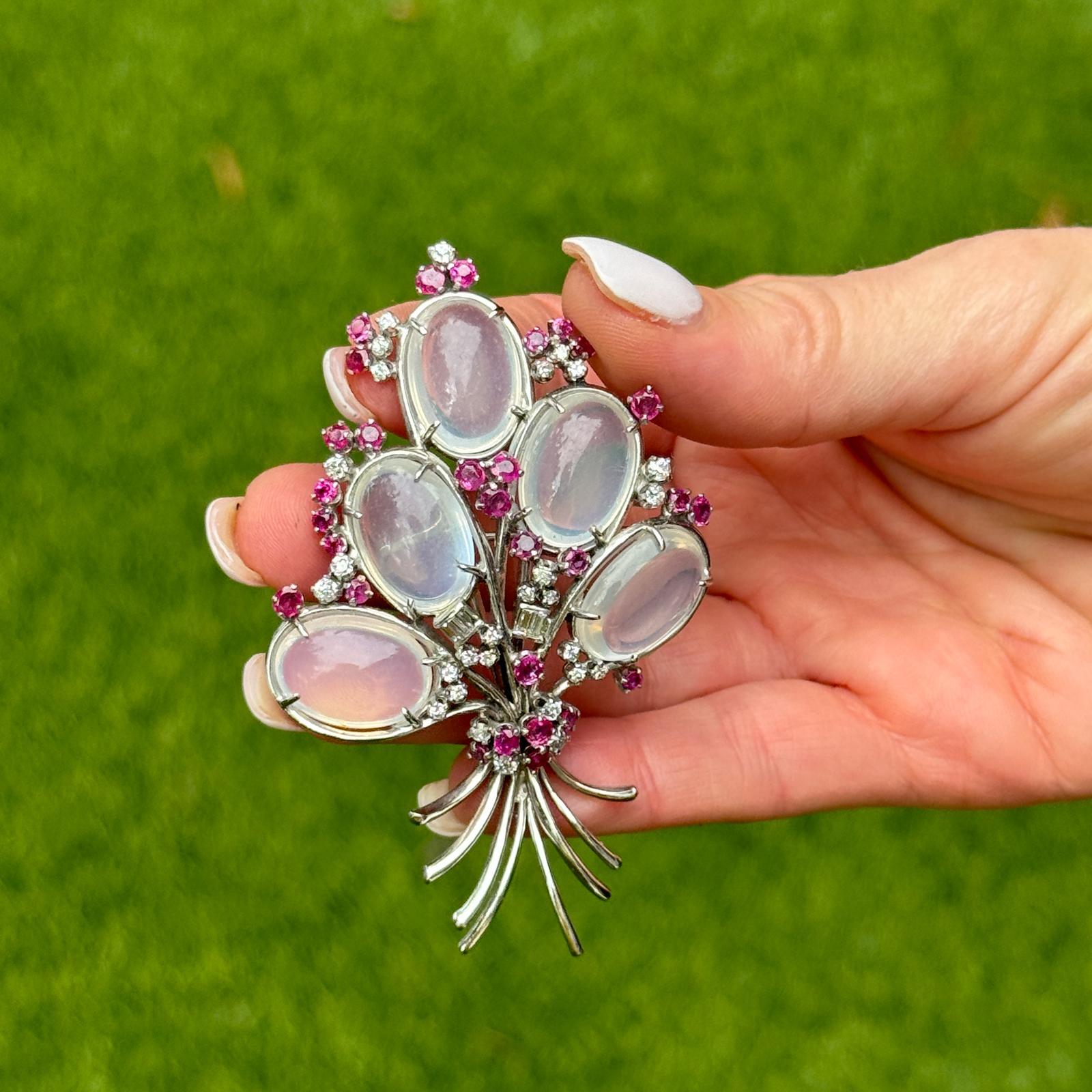 Diese aus der Mitte des 20. Jahrhunderts stammende Brosche aus 14-karätigem Weißgold besticht durch eine zauberhafte Kombination aus Mondstein, Diamanten und Rubinen in einem raffinierten und eleganten Blumendesign. Die Brosche ist mit 28 Old