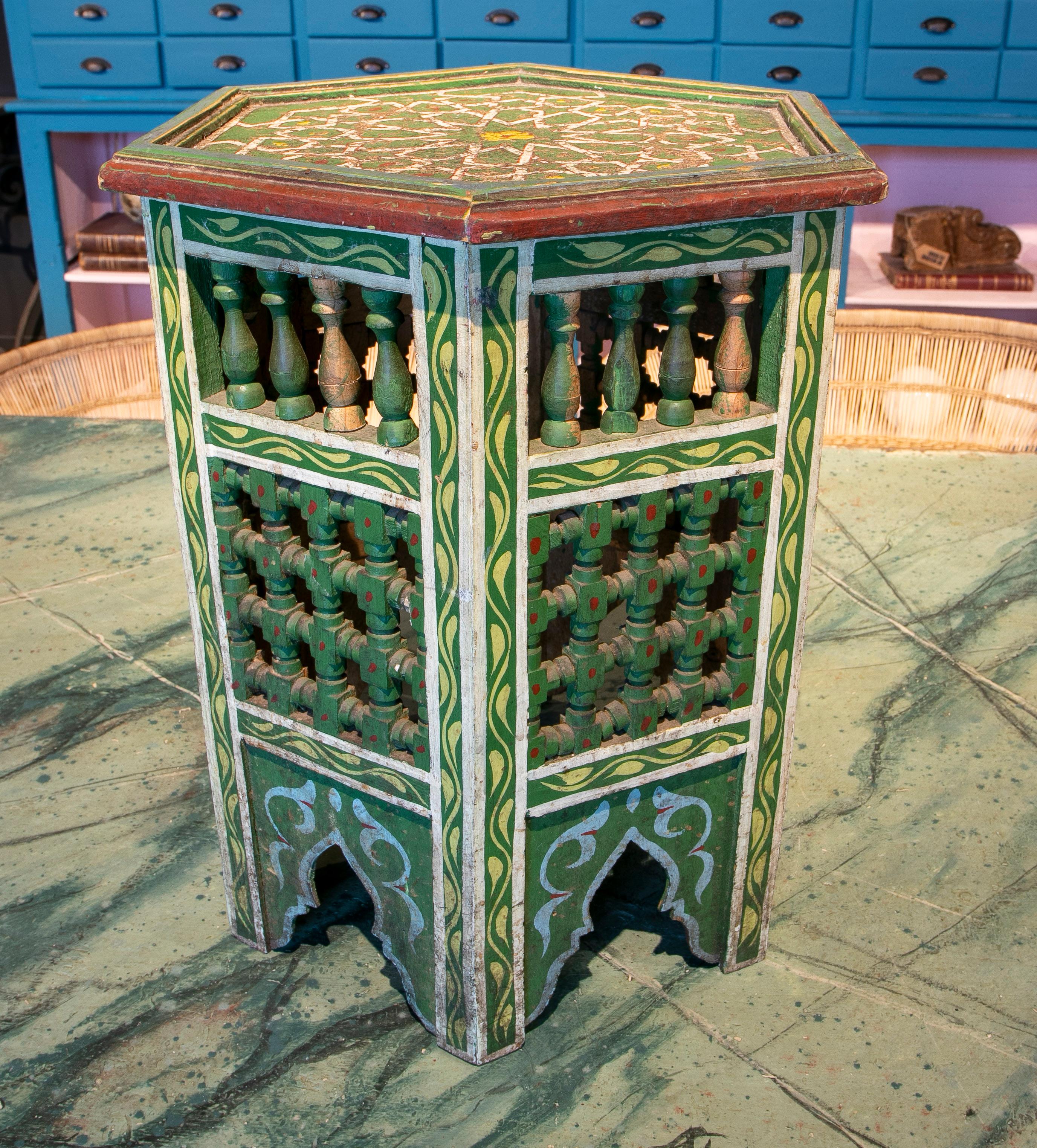 Vintage 1970s Moroccan hand-painted green hexagonal wooden pedestal table with floral and geometric designs in traditional Mediterranean colours, decorated with wooden spindles, Moucharabie fretwork and arches on the base.

African folk Art