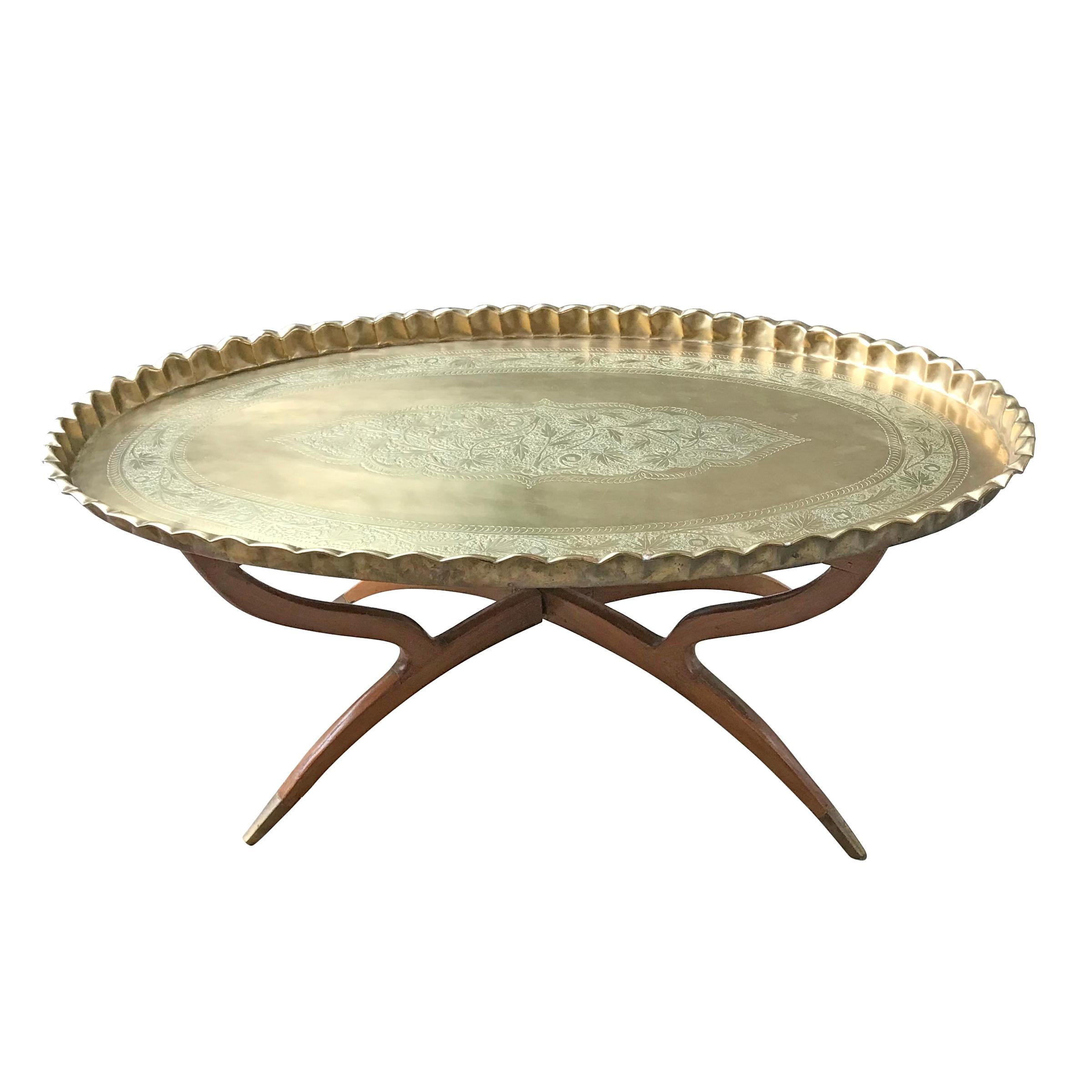 A wonderful mid-20th century Moroccan tea table with a large heavy brass oval tray with hand-chased floral decorations and ruffled rim, mounted on a folding four-legged mahogany stand with brass feet.