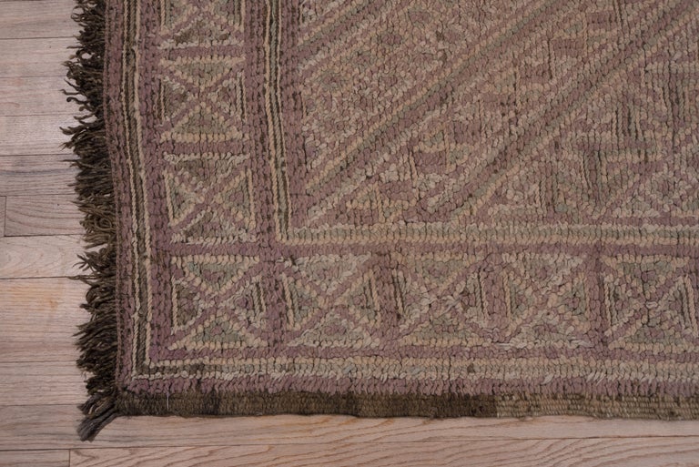 The mauve field shows a large lozenge pattern detailed in ecru, with internal squares and other geometric devices. Narrow border of squares quartered into triangles. Red wool fringes. Good condition.
  