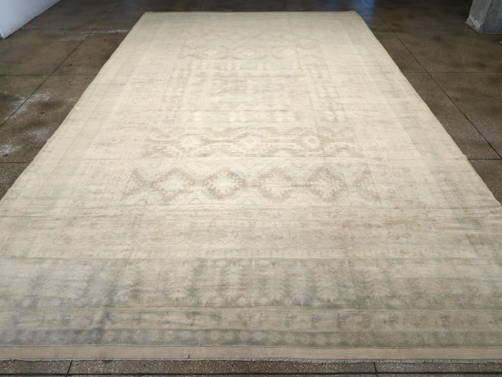 A wool pile of symmetric knots on a cotton foundation. This extra-large Moroccan town piece features a strongly muted palette with geometric design elements in straw, beige, light rust and smoke, adapted from Turkish rugs. The pale brown main border