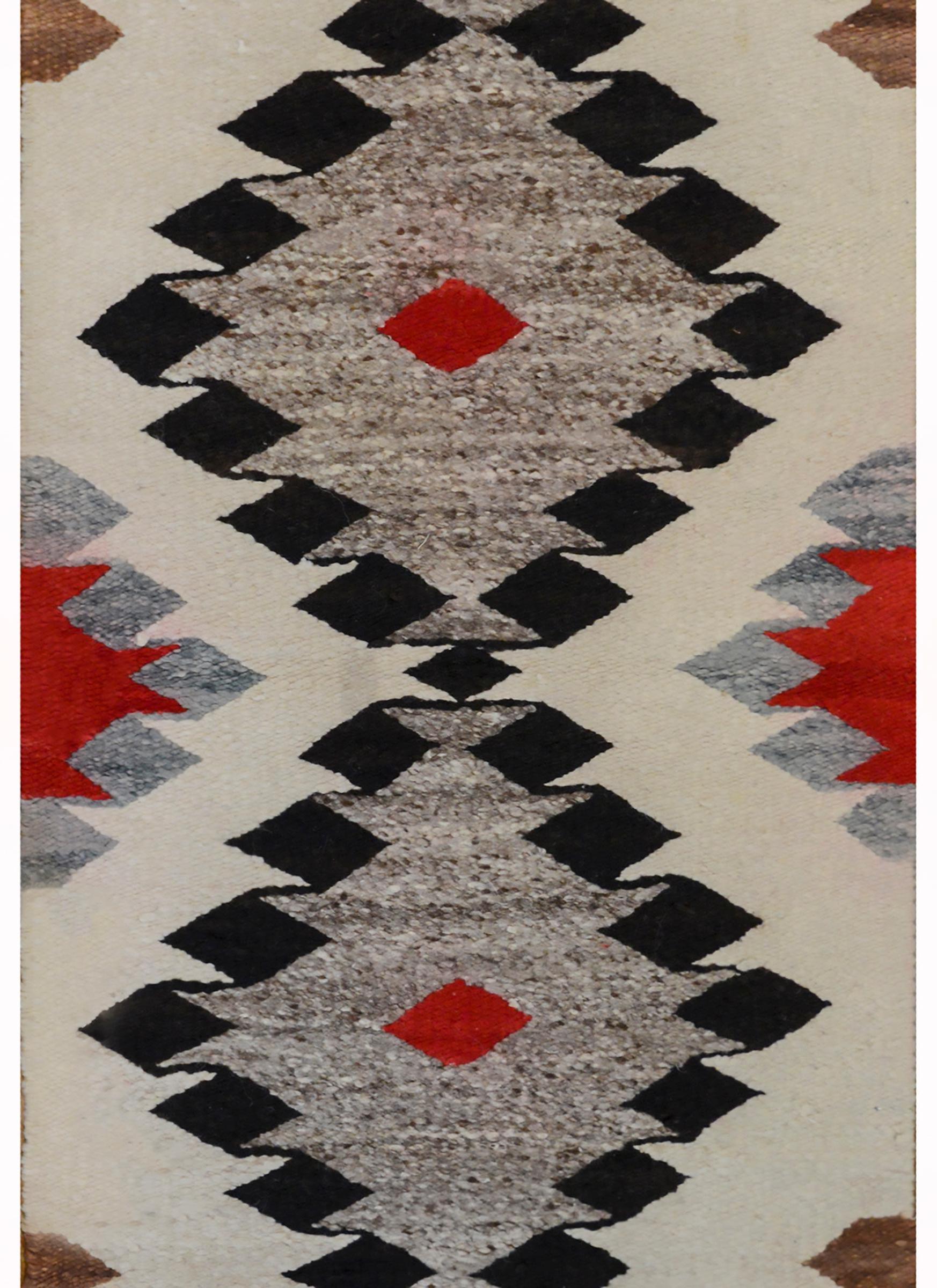 Ein kräftiger Navajo-Teppich aus der Mitte des 20. Jahrhunderts mit zwei großen schwarzen, grauen und purpurroten Rauten auf einem cremefarbenen Feld mit weiteren kleineren Rauten.