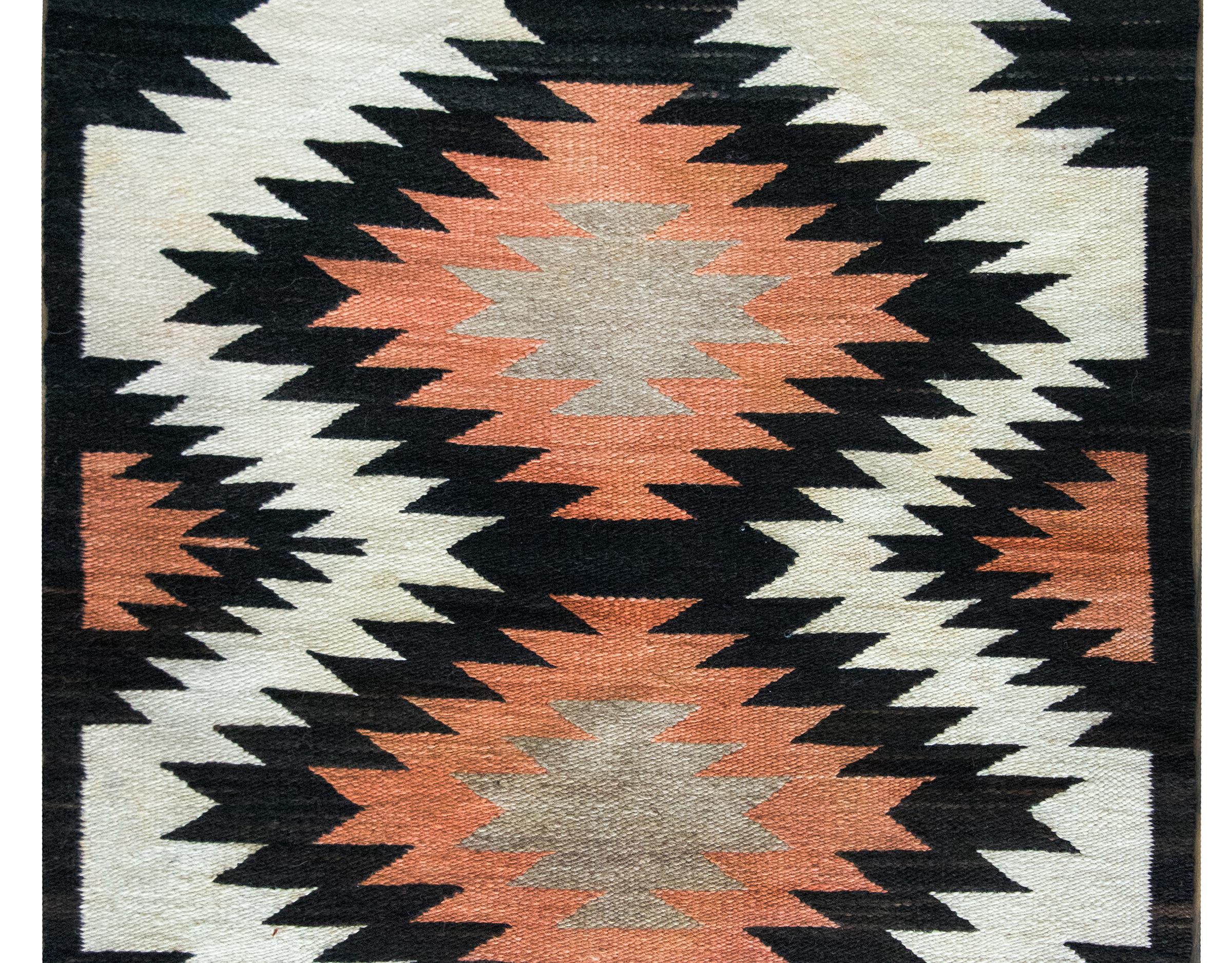 A striking mid-20th century Navajo rug with two large diamond medallions woven in black, red, and brown wool, living amidst a field of white, and flanked by more black and red designs.  