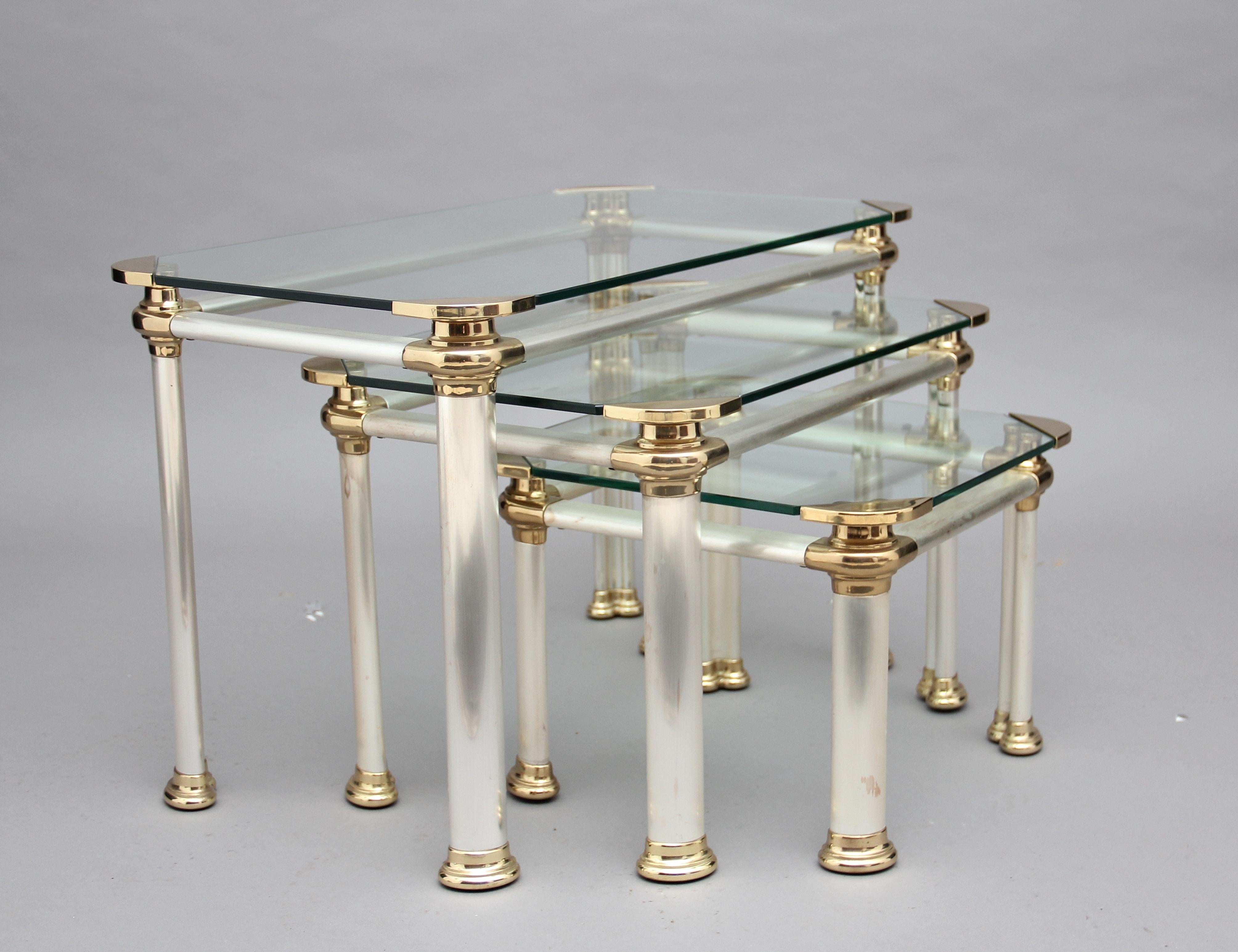A nest of three mid-20th century Italian brushed steel, brass and glass occasional tables, having a glass top with decorative brass corners, a brushed steel frame and oval legs ending on brass caps. Lovely quality and in excellent condition, circa