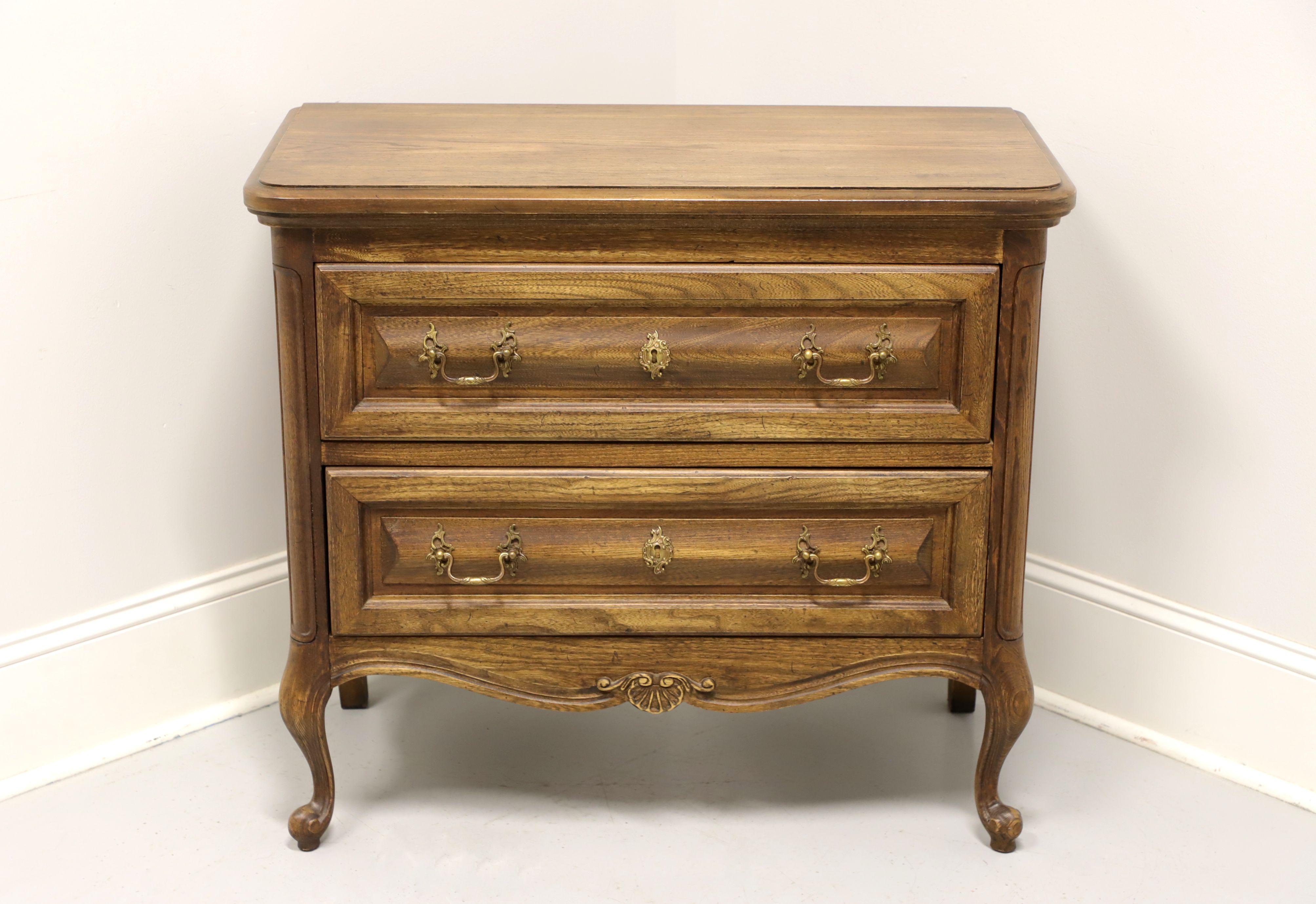 A French Country style occasional chest, unbranded, similar quality to Century or Henredon. Solid oak with brass hardware, carved apron, slender curved front legs and scroll feet. Features two drawers of dovetail construction with faux keyhole