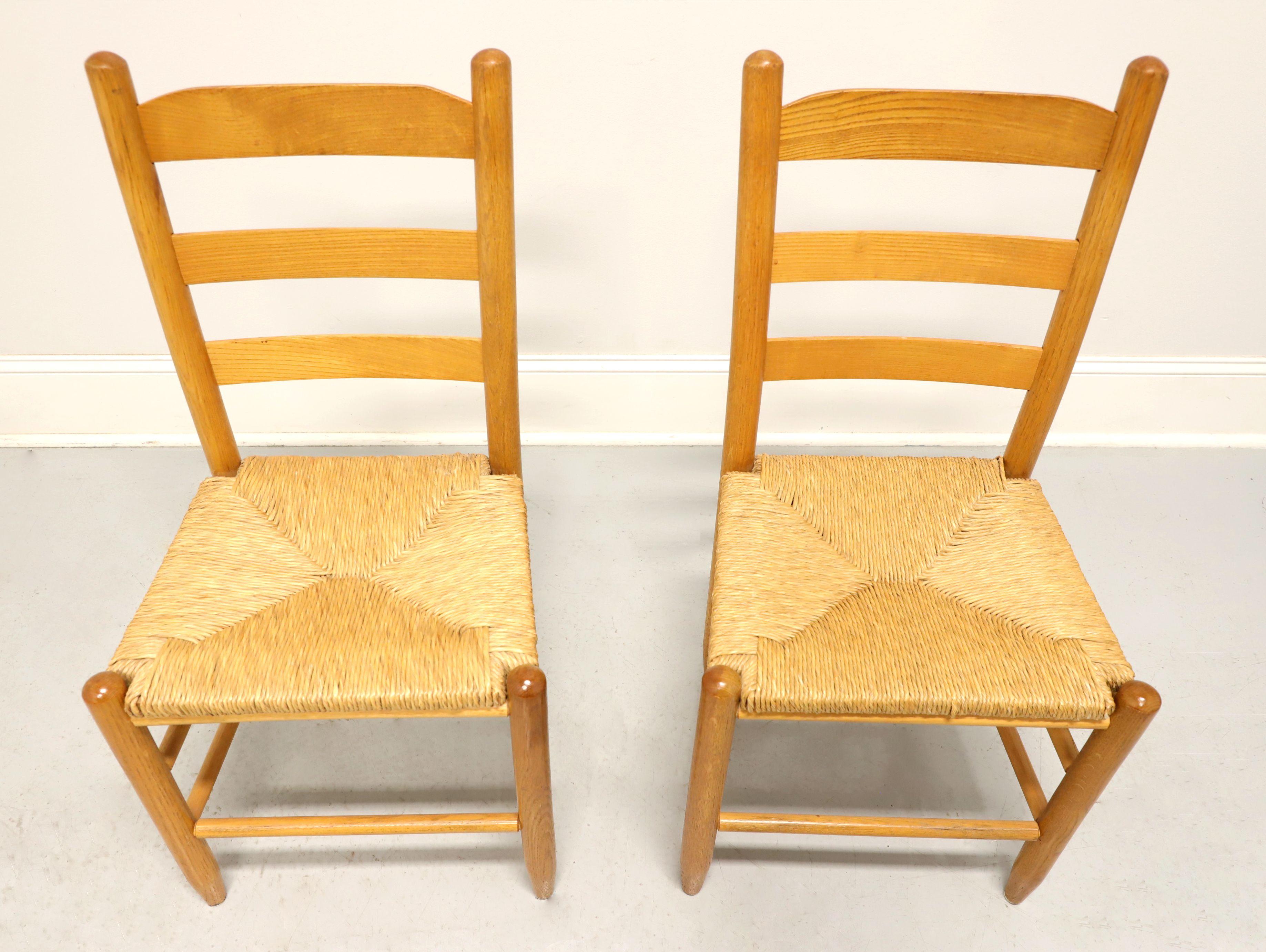 A pair of cottage style dining side chairs, unbranded. Solid oak with ladder back design, rush seats, tapered round legs and stretchers. Made in the USA, in the mid 20th century.

Measures: Overall: 17.5 W 17 D 35.5 H, Seat: 16.75 W 14 D 18