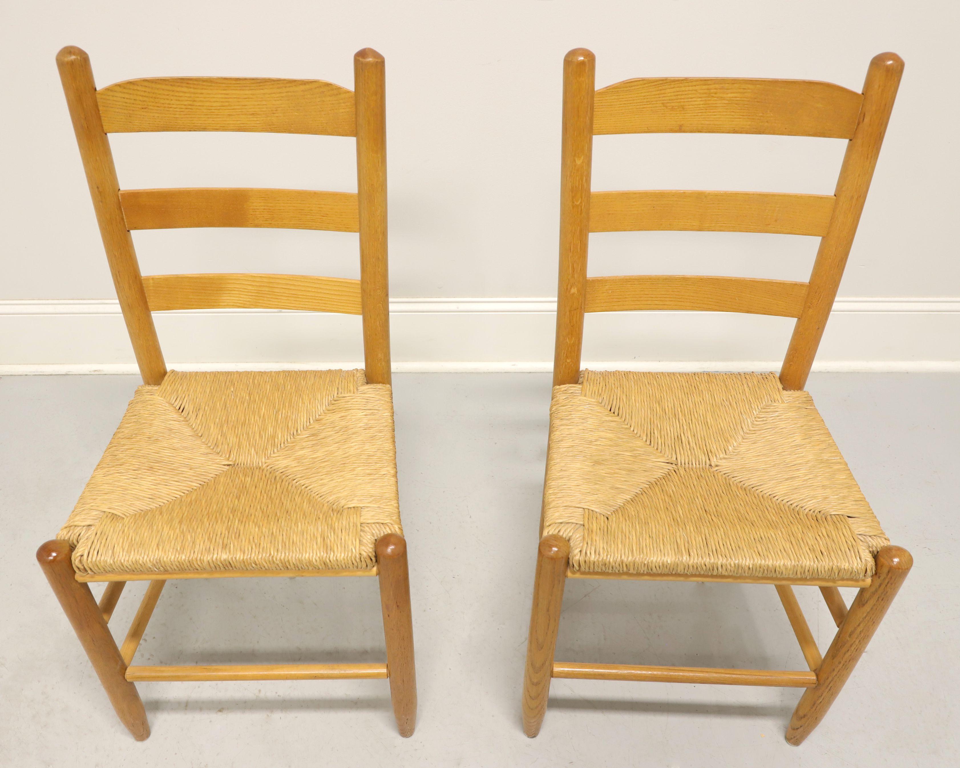 A pair of Cottage style dining side chairs, unbranded. Solid oak with ladder back design, rush seats, tapered round legs and stretchers. Made in the USA, in the mid 20th Century.

Measures: Overall: 17.5w 17d 35.5h, Seat: 16.75w 14d