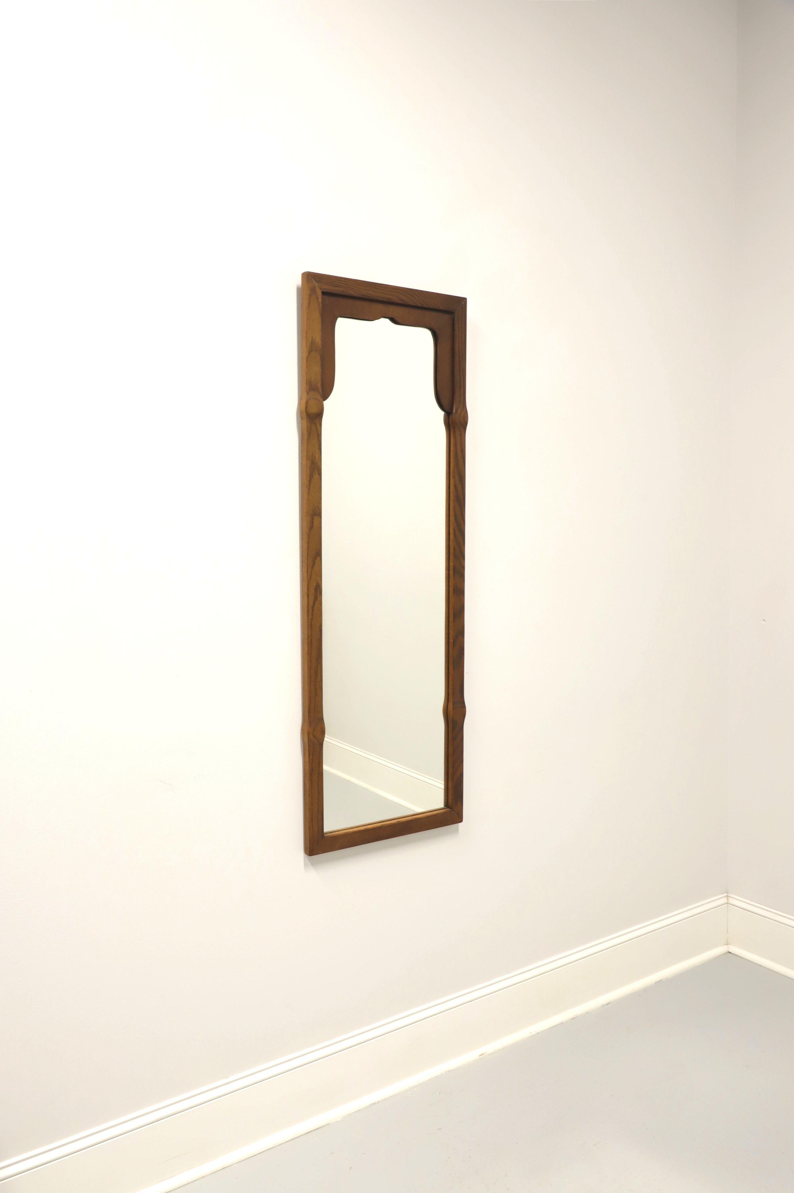 A Regency style wall mirror, unbranded, similar quality to Tomlinson. Mirrored glass in an oak wood rectangular frame with slight rounding at four points. Features an arched dark walnut insert to inside top of the oak frame. Made in North Carolina,