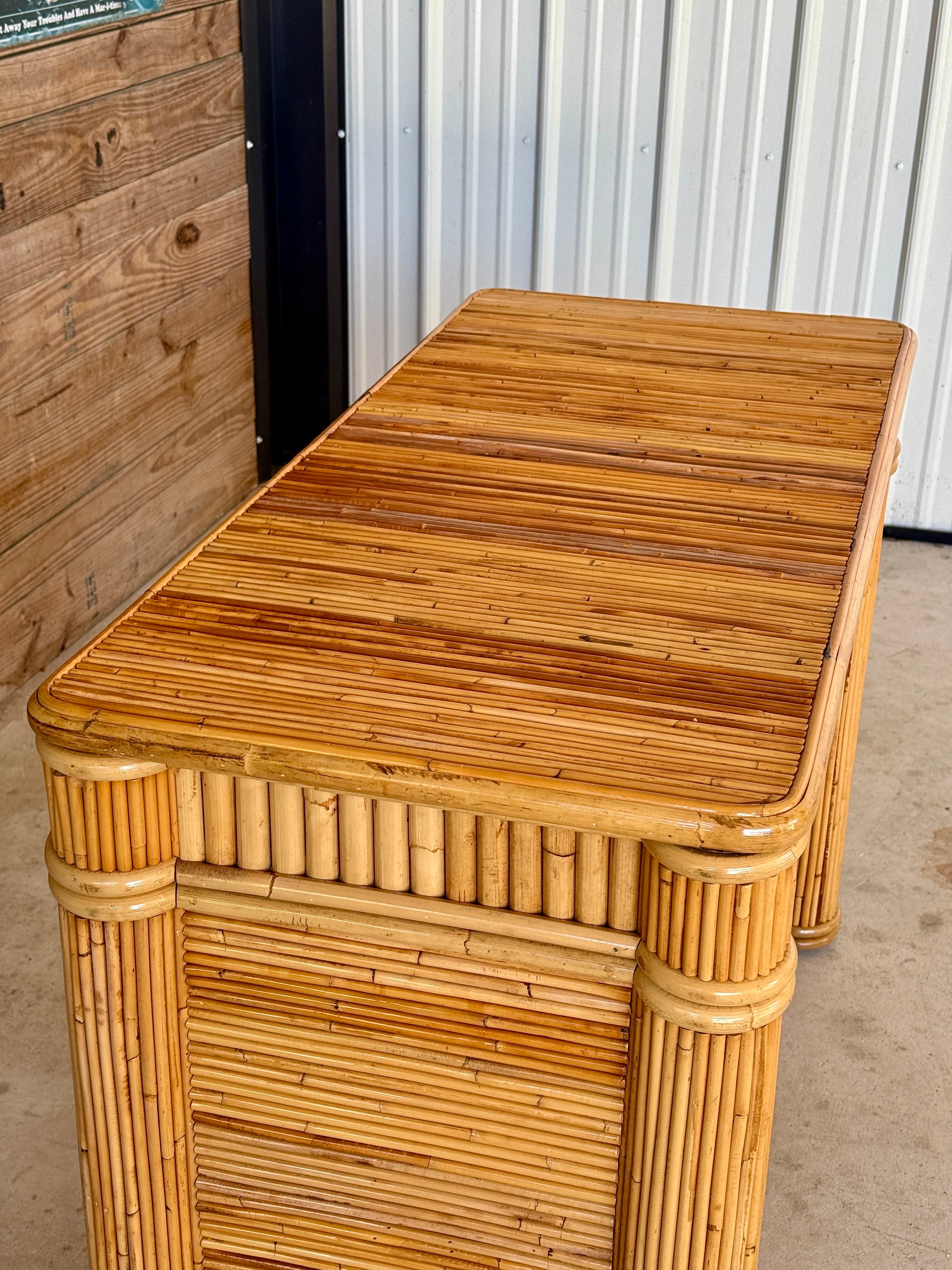 A stunning Mid-20th Century pencil reed rattan and bamboo desk featuring a streamlined design with rounded edges and a single center drawer.
The piece showcases intricate craftsmanship with tightly wrapped rattan and bamboo paneling, adding texture