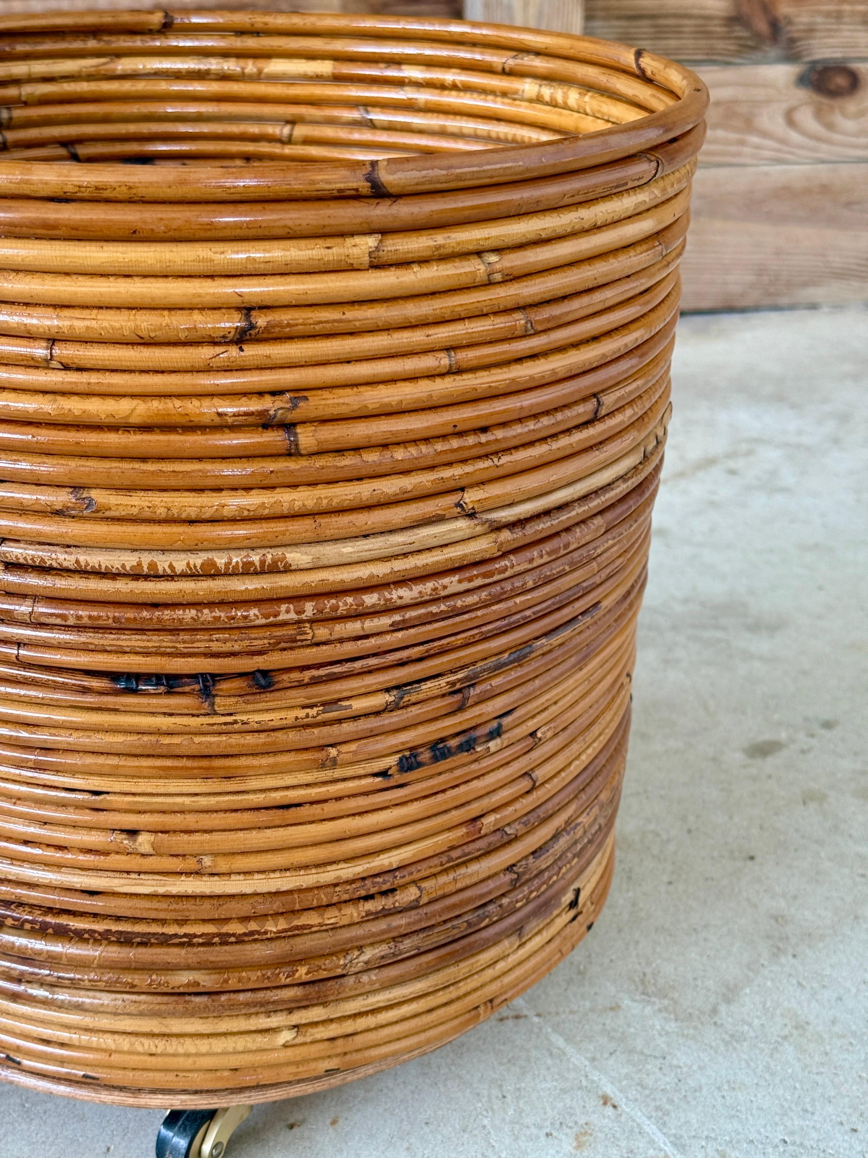A versatile mid-20th century pencil rattan cylinder form on brass wheels, lightly refinished to bring out its natural golden tones. This piece works beautifully as a rolling planter for a palm or fiddle leaf fig but could also serve as a stylish
