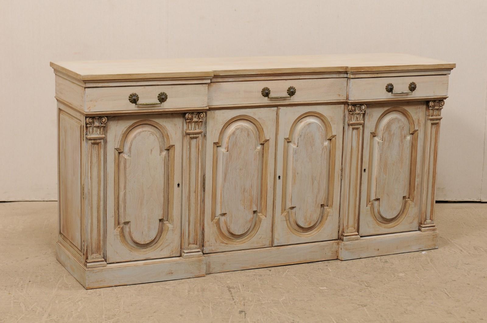 An American painted and carved wood buffet cabinet from the mid-20th century. This vintage American credenza, approximately 6 feet in length, features three drawers atop four raised paneled doors, with arched tops and bottoms, of which are flanked