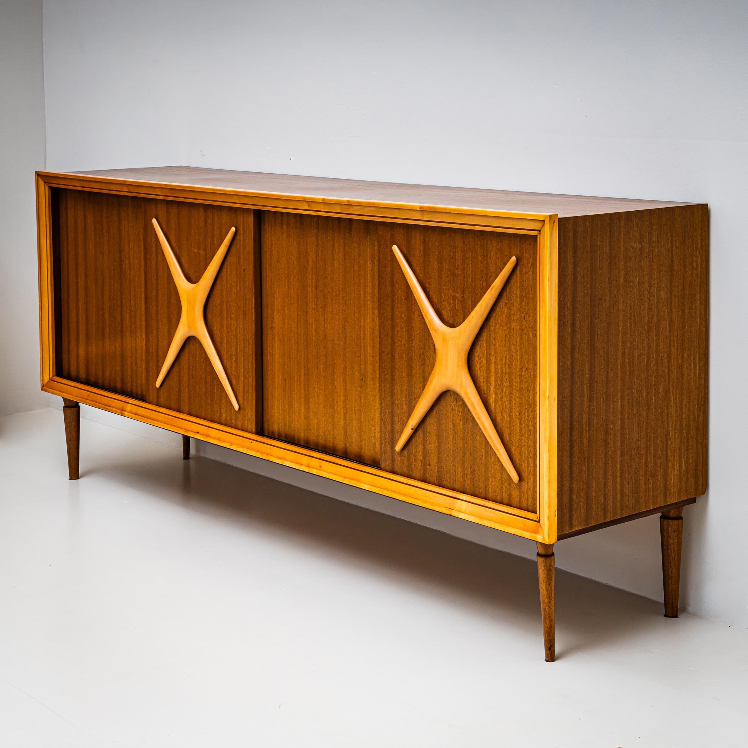 Zwei elegante italienische Sideboards mit Schiebetüren und dekorativen X-förmigen Reliefs aus hellem Holz. Jedes Stück steht auf spitz zulaufenden Beinen und ist mit einer hellen Umrahmung versehen. Die Innenräume sind mit Regalen und Schubladen