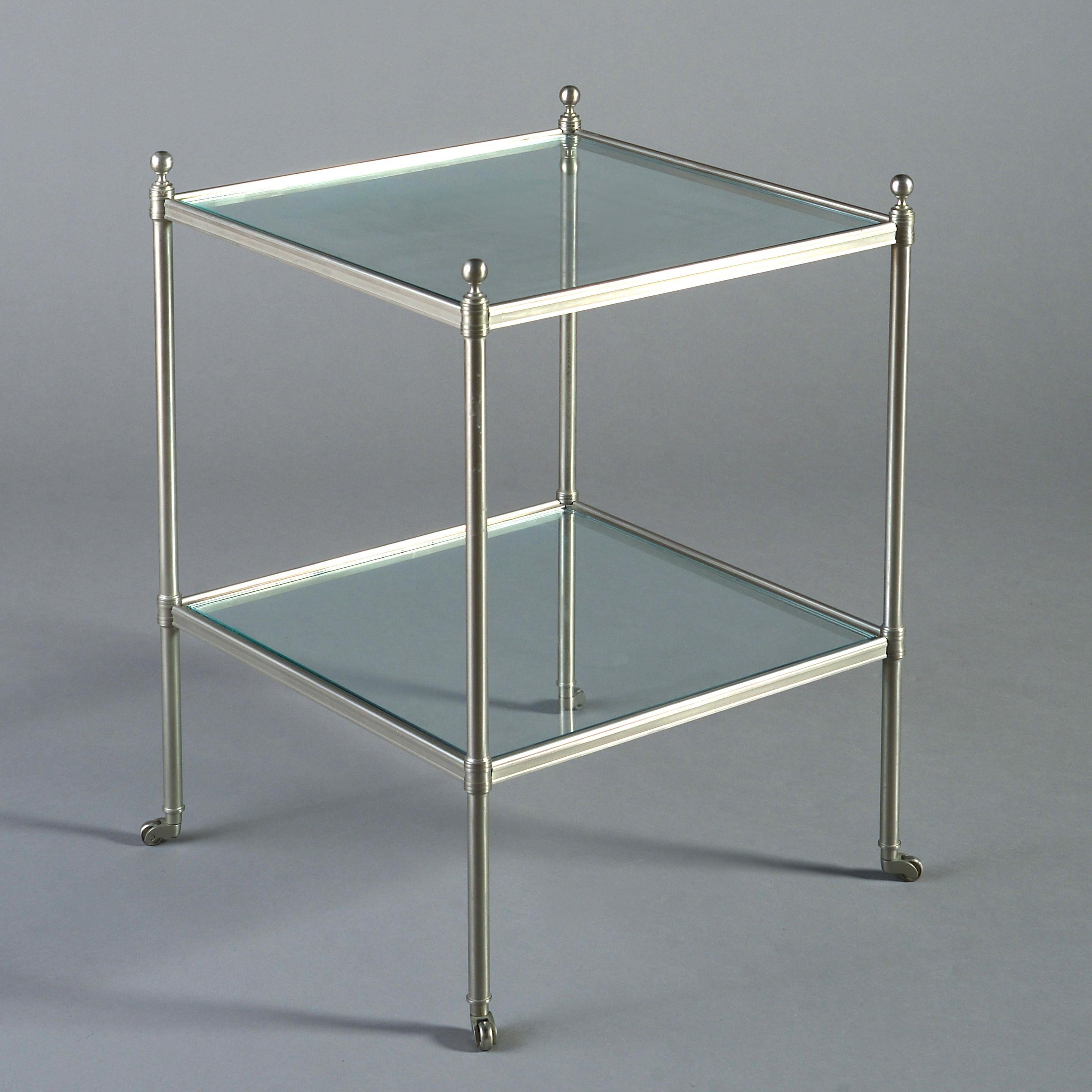 A pair of mid-20th century steel two-tier tables, each having square glass shelves and raised upon tubular legs with ball finials and terminating in castors.