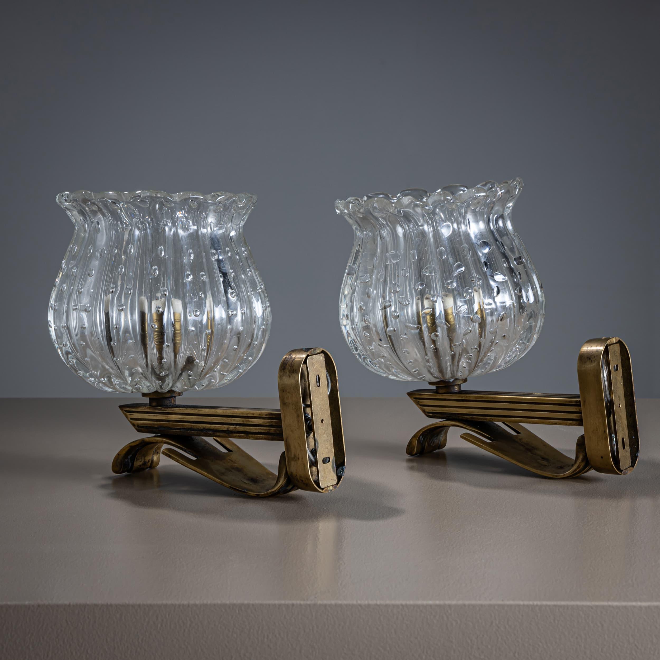 Paire d'élégantes appliques murales avec des montures en laiton finement travaillées. Les abat-jours en verre clair en forme de tulipe présentent de délicates bulles d'air décoratives, ajoutant une touche de légèreté et de raffinement. Les pièces
