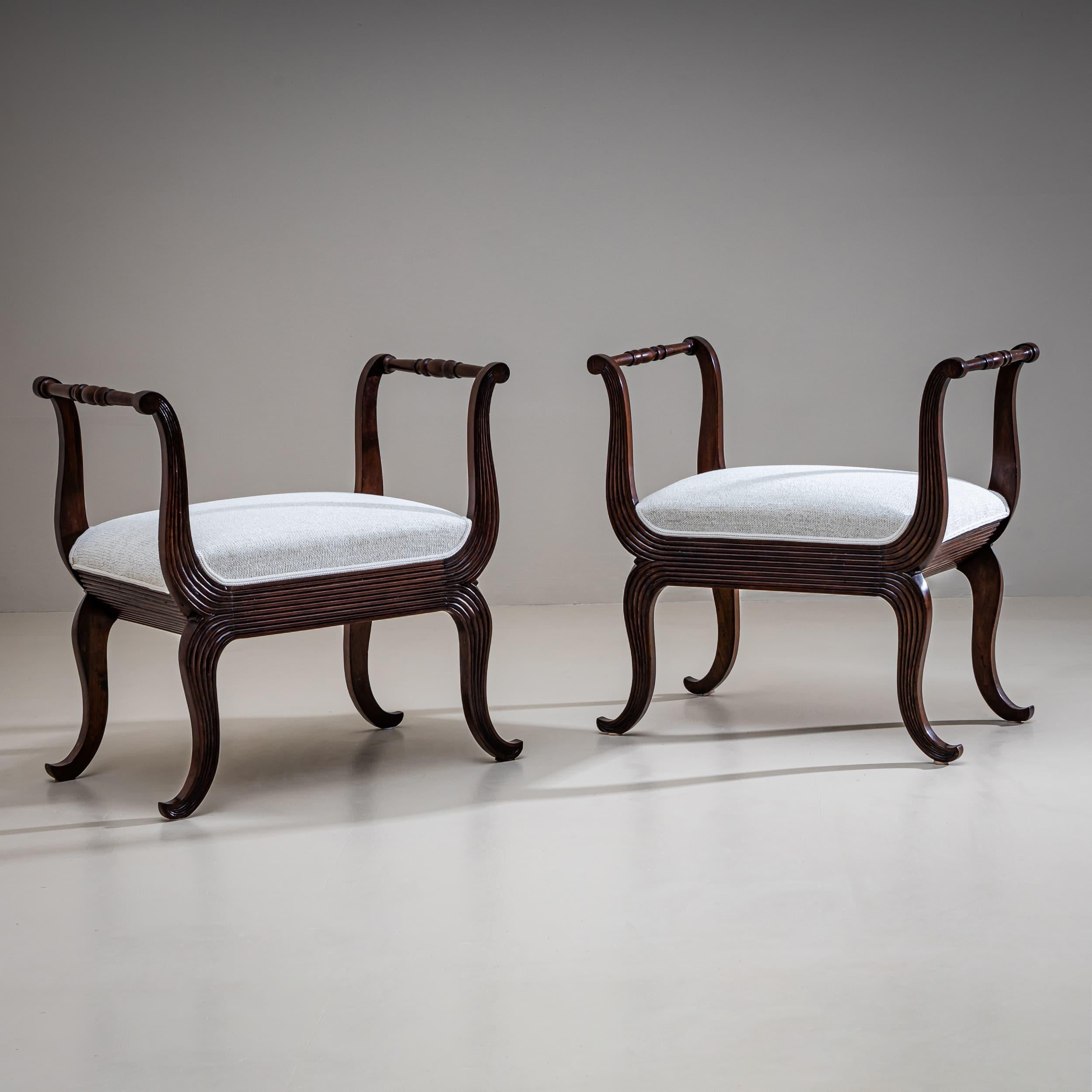 Pair of tabourets crafted from walnut, featuring curved armrests and legs with fluted details. The armrests are connected by a turned stretcher. Expertly restored and newly upholstered in a white woven fabric.