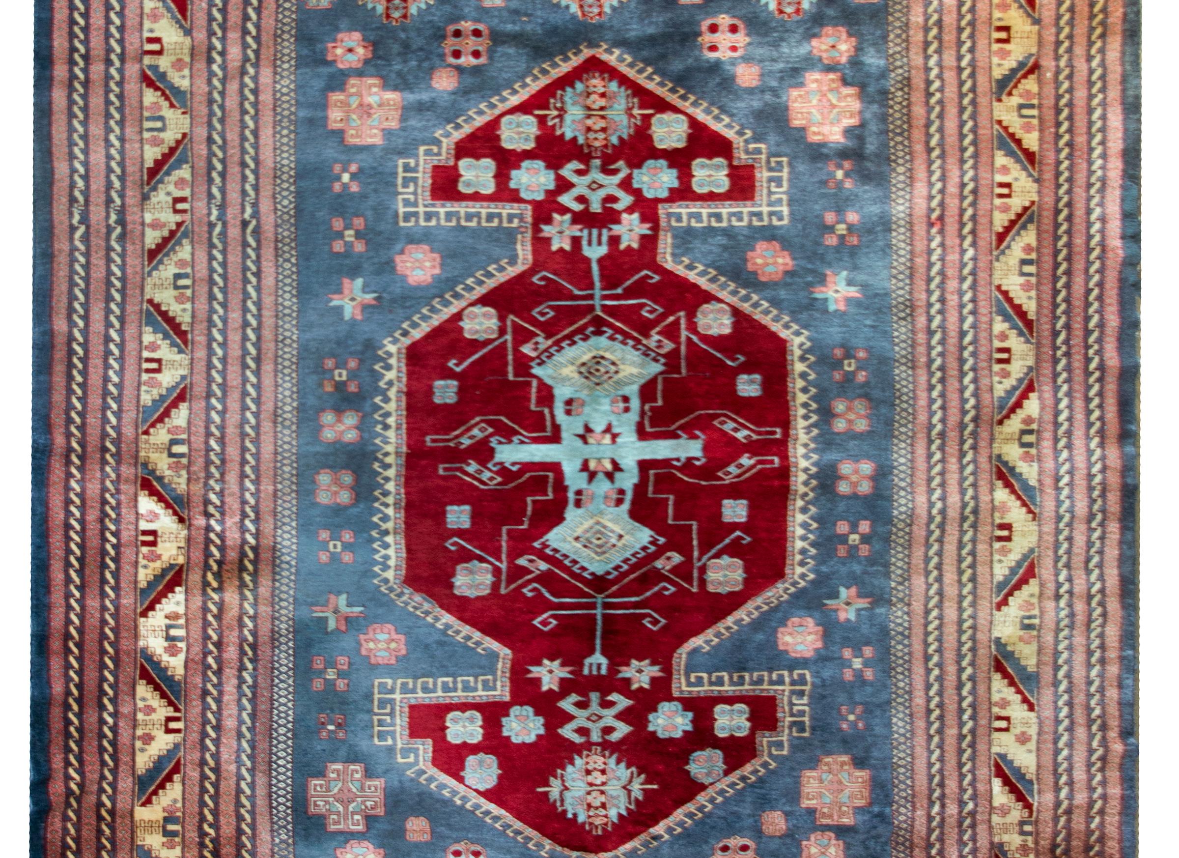 A wonderful mid-20th century Pakistani Bokhara rug with a large central medallion living amidst a field of stylized flowers all woven in pink, cranberry, and light indigo, and all surrounded by a complex border containing various petite geometric