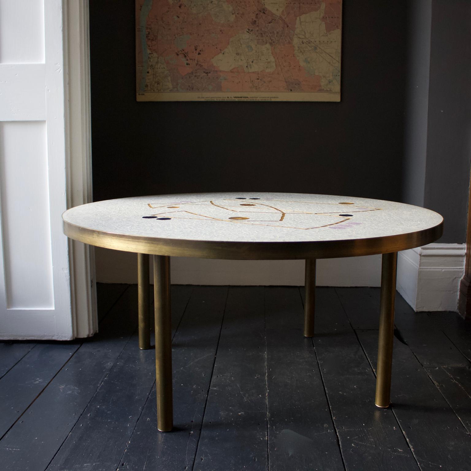 Mid-20th century modern pale grey mosaic table with gold and lilac accents and brass surround.

The tabletop is covered in pale grey mosaic with a beautiful abstract pattern of gold lines and circles, with black and lilac accents. The mosaic is