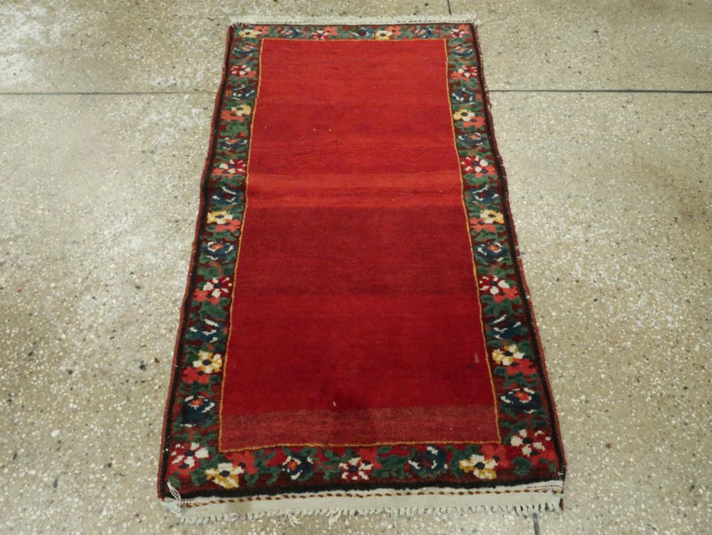 Un tappeto persiano vintage Bakhitiari. Il campo rosso, completamente liscio e ben abraso, è incorniciato da un bordo marrone scuro ricoperto da fiori e foglie. La striscia di rosso più chiaro che attraversa il centro è un tocco particolarmente