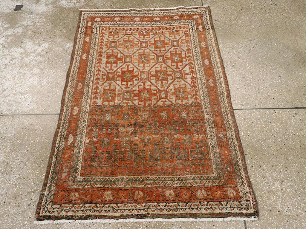 Un tappeto persiano Baluch vintage. Il fondo cammello abraso di questo spargimento tribale persiano orientale presenta un motivo a reticolo ottagonale e quadrato piccolo allover con quadrati uncinati color ruggine nelle riserve più grandi, mentre il