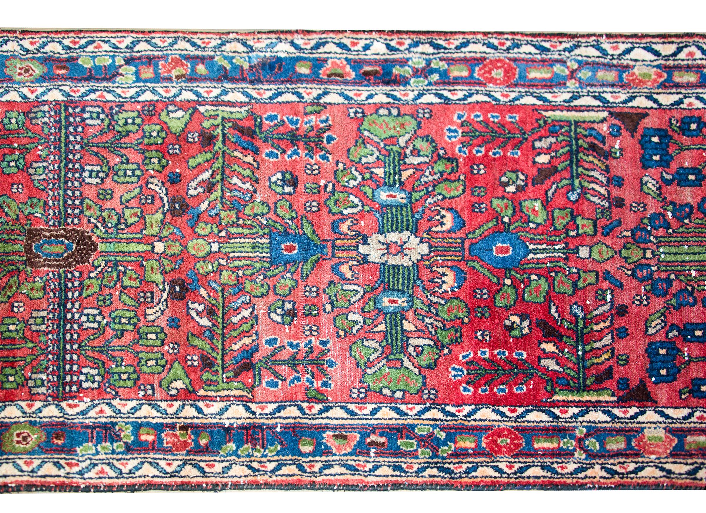 A wonderful mid-20th century Persian Dargazin runner with a mirrored stylized floral and vine pattern woven in lime green, indigo, peach, and indigo, set against a dark crimson background, and surrounded by a complex border with simple stylized