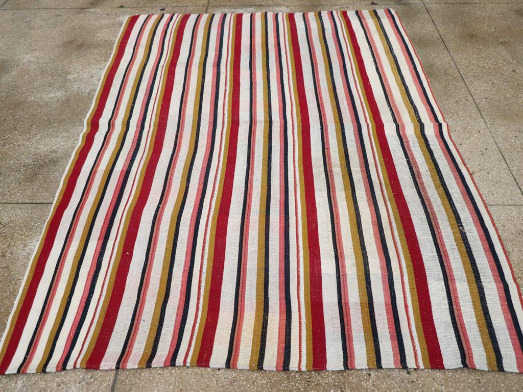 Esta alfombra Kilim turca de tejido plano de mediados del siglo XX, que mide 1,70 m x 1,80 m, muestra una animada composición de atrevidas rayas verticales en una paleta vibrante y alegre. Las bandas alternas de rojo, rosa, amarillo, marfil, verde y