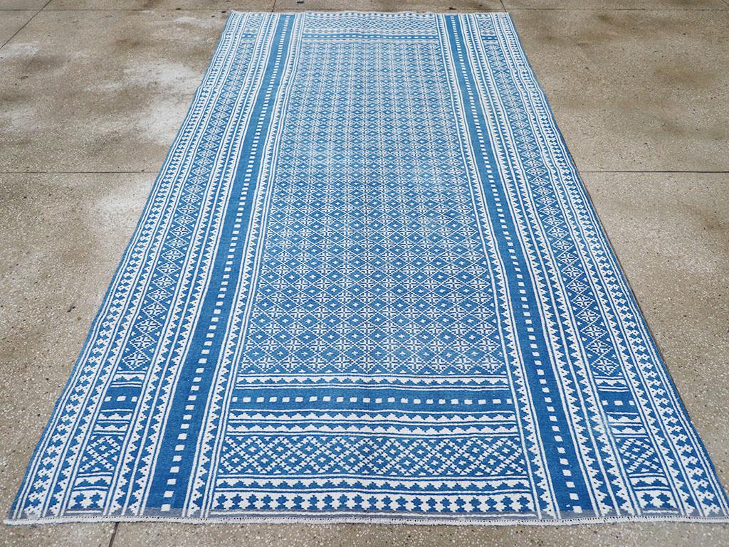 Zilu-Schuss-Technik in Baumwolle. Dieses dichte blau-weiße Flachgewebe weist ein Feld aus kleinen Quadraten und Rauten auf, das von durchgehenden Seiten- und kurzen Endbordüren mit verschiedenen bitonalen Mosaikmustern eingerahmt wird. Das Stück ist