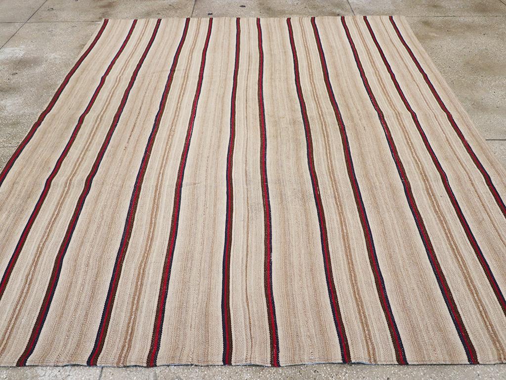 Esta alfombra kilim persa de tejido plano de mediados del siglo XX, que mide 2,8 m x 2,8 m, presenta un refinado diseño lineal con rayas estrechas y atrevidas alternadas. El cálido fondo marfil se acentúa con rojo intenso y sutiles bandas de tonos