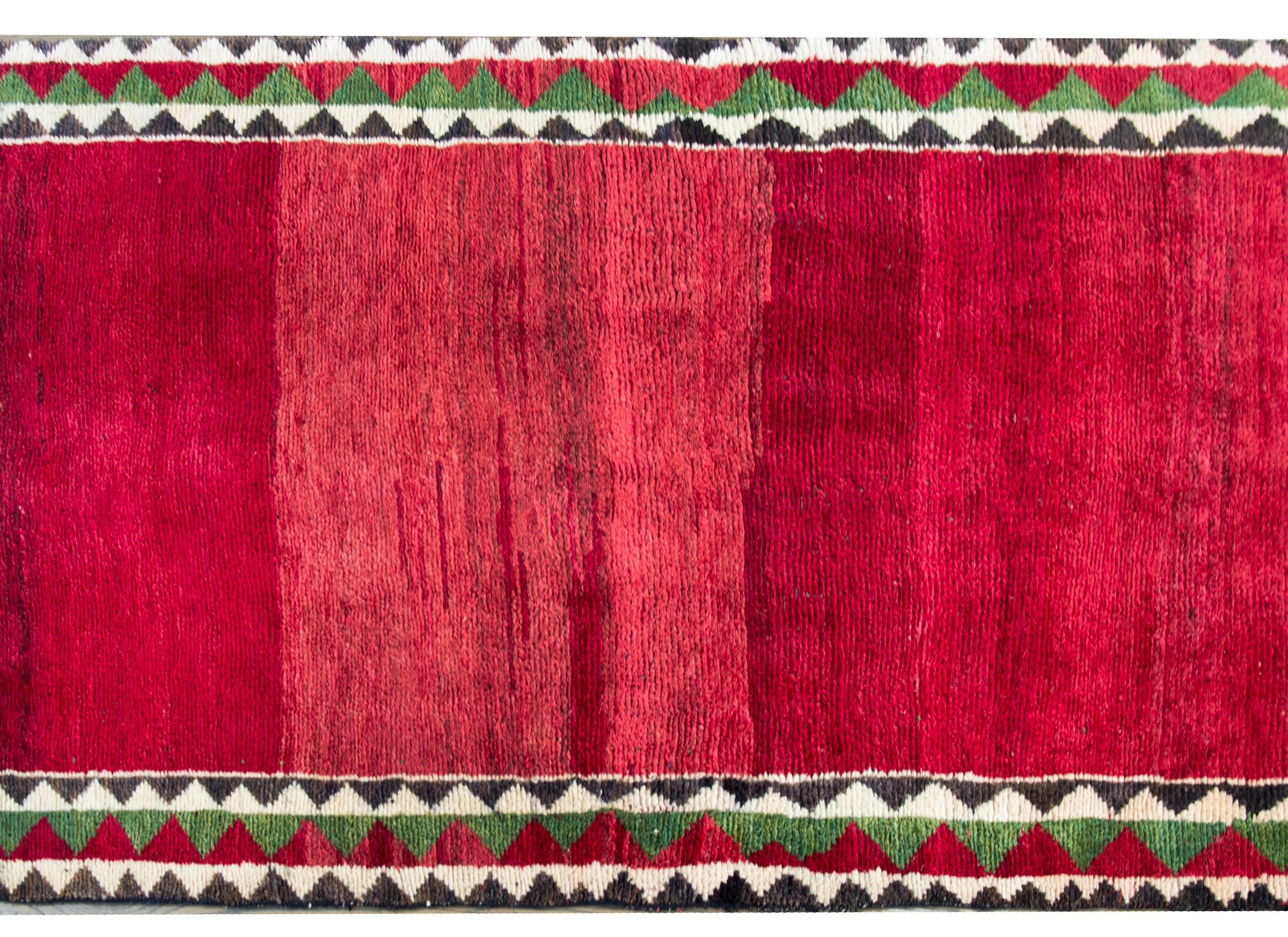 An incredible vintage Persian Gabbeh rug with a wonderful abrash crimson field surrounded by a geometric patterned border with alternating white, brown, green, and crimson triangle stripes.